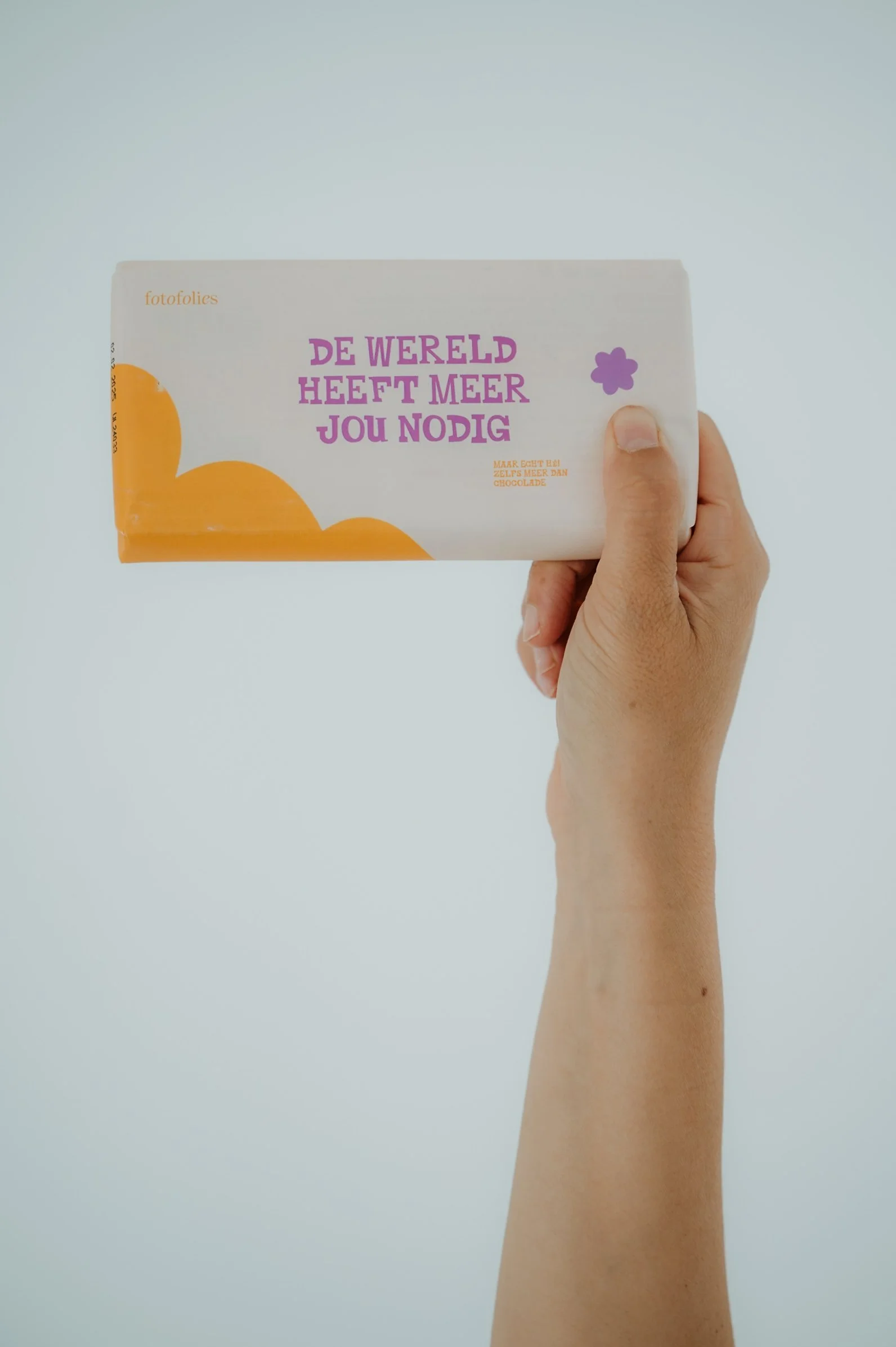 Hand holding a white chocolate bar with Dutch text and a small purple flower design, against a plain light background.