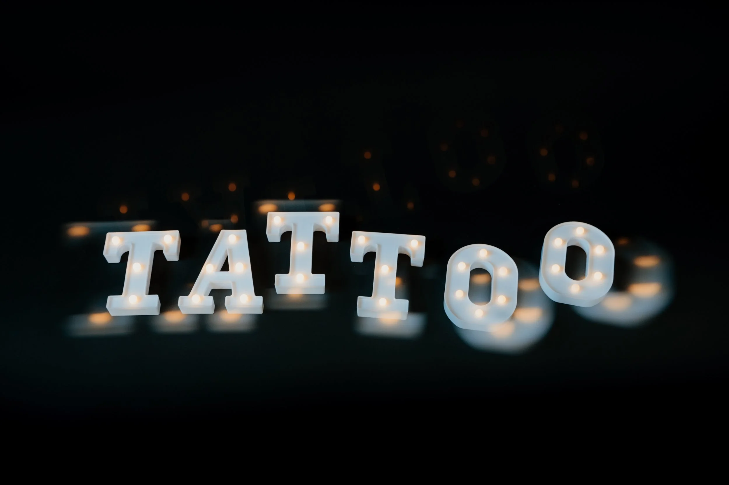 Illuminated letters spelling 'TATTOO' on black background.