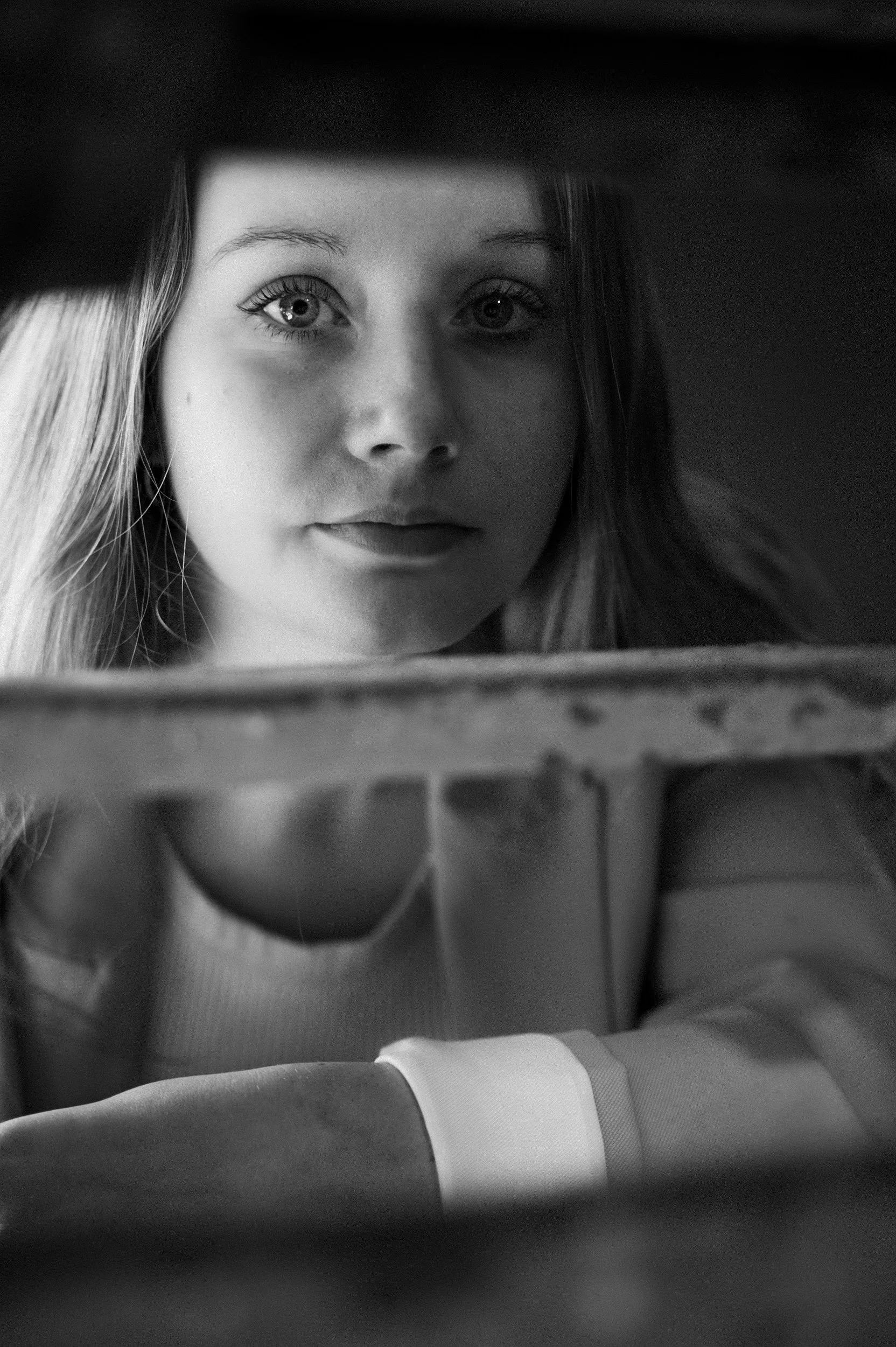 A young woman with long hair looking into a mirror, taking a selfie with a camera or phone, with a thoughtful expression.
