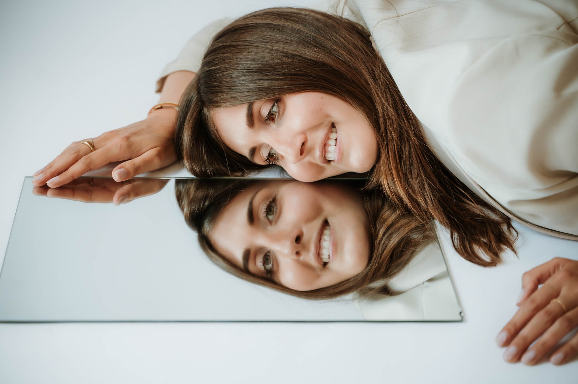 A woman with long brown hair smiling and touching a mirror with her finger.