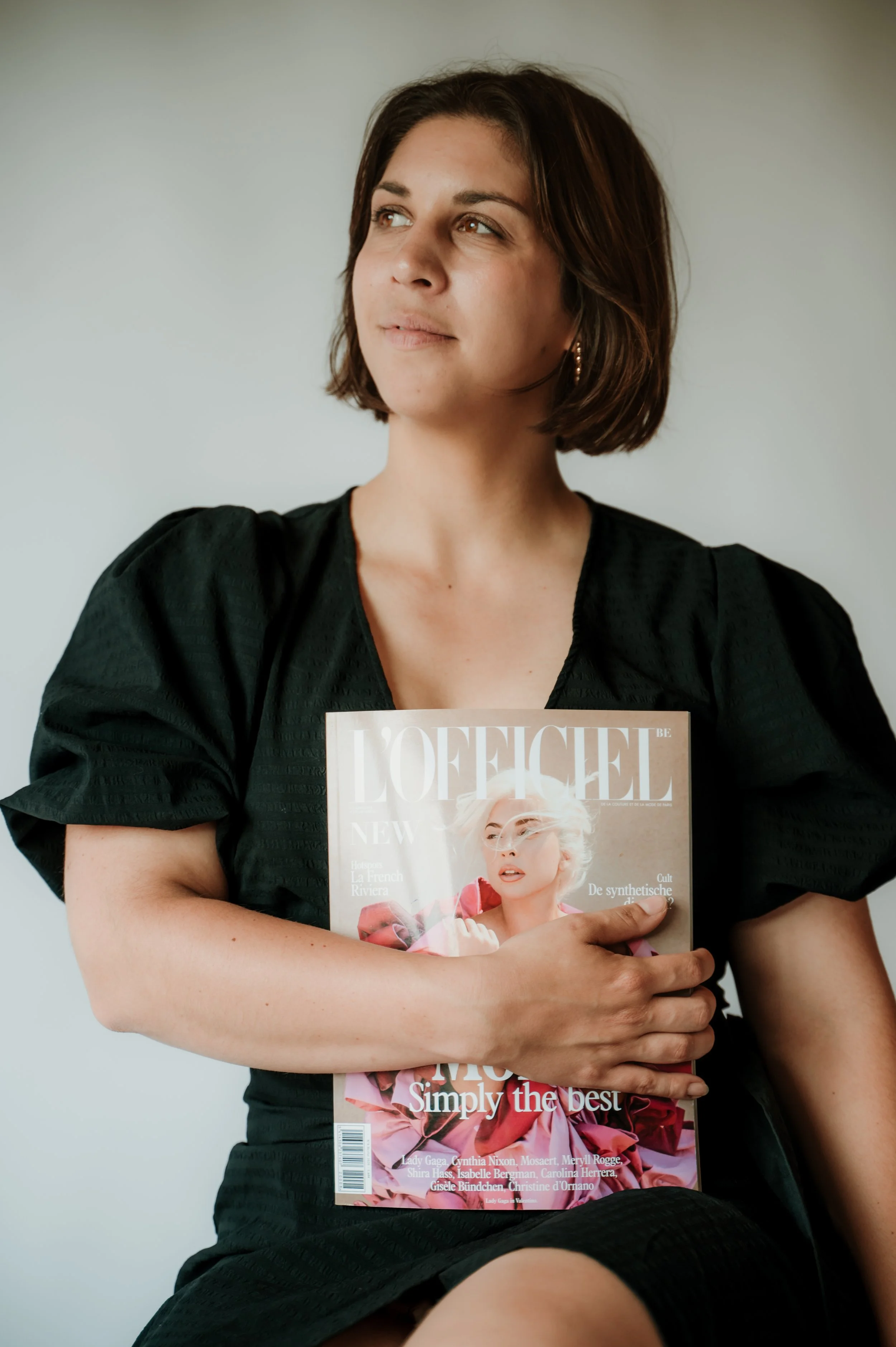 A woman with short brown hair holding a Vogue magazine featuring a woman with short platinum blonde hair and pink flowers on the cover.