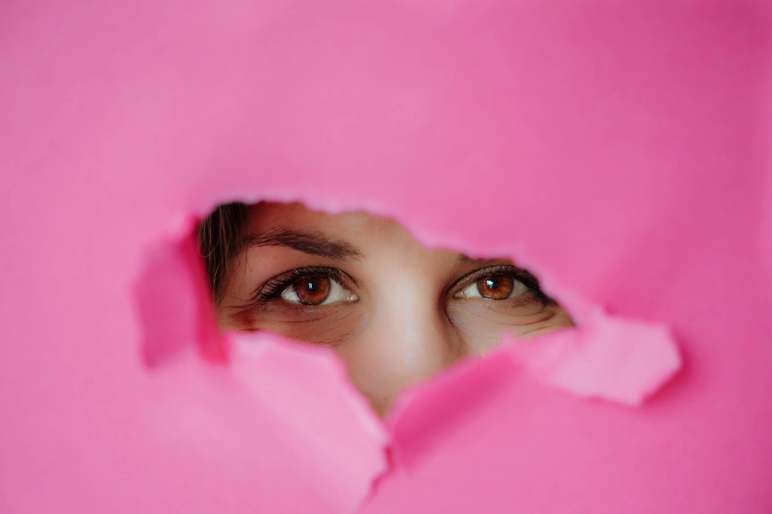 Person looking through a pink heart-shaped hole, with only their eyes and part of their forehead visible.