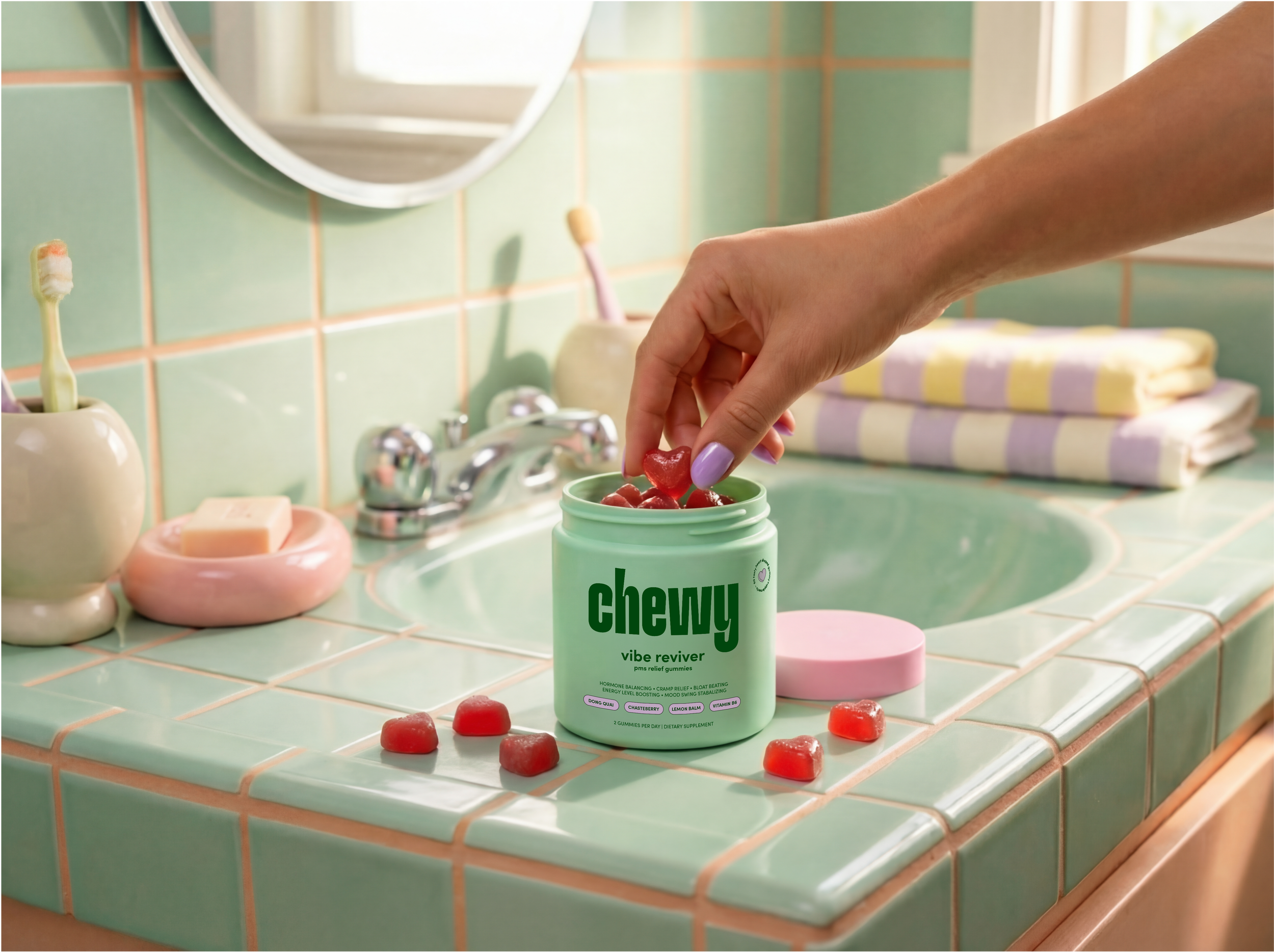 A bathroom countertop with a green container of gummy vitamins labeled 'chewy vibes reviver' and several red gummy candies spilled on the counter. The background shows a pastel green tiled wall, a mirror, and a bottle of toothbrushes.
