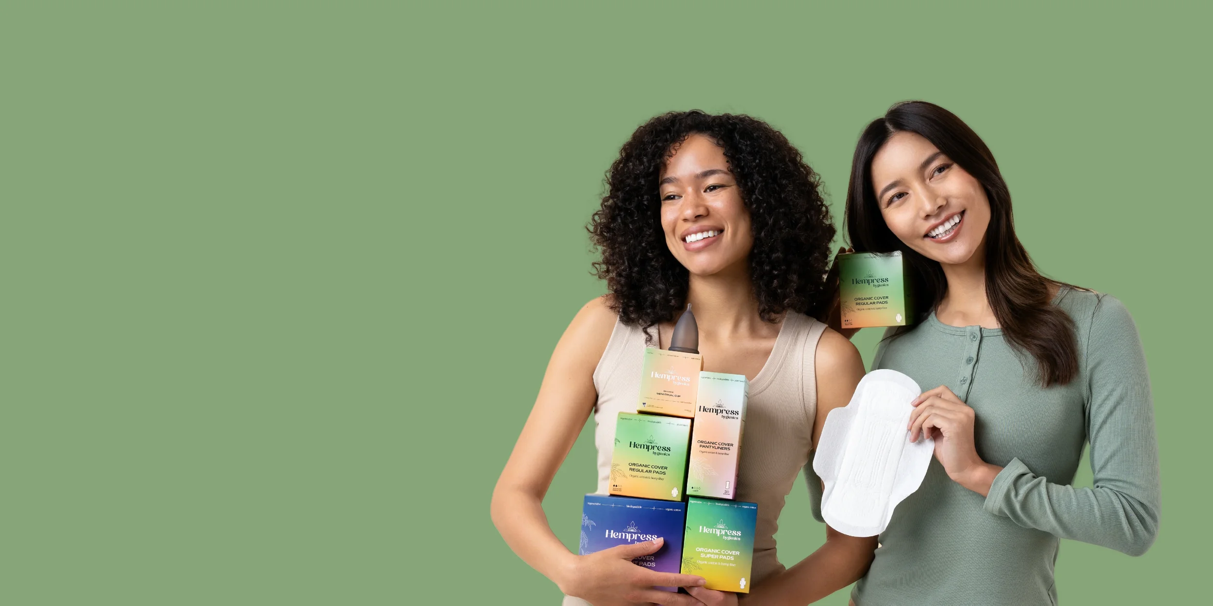 Two women smiling, holding various hemp pads and products with a green background.
