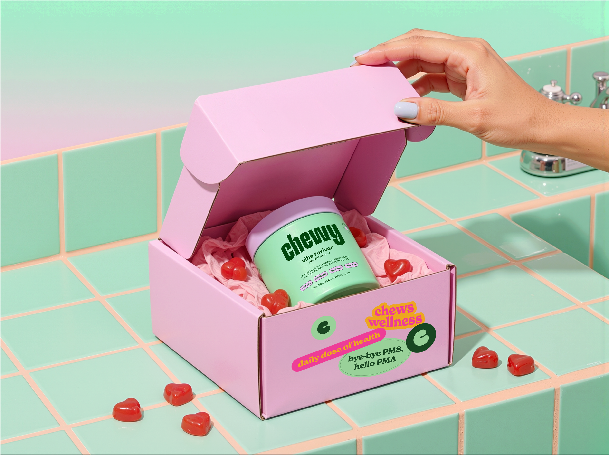 A pink box labeled "chews wellness" on a pastel tiled bathroom countertop. The box contains red gummy vitamins shaped like hearts. A hand is opening the box, revealing the gummies inside. The box has additional text about health benefits and ingredients.