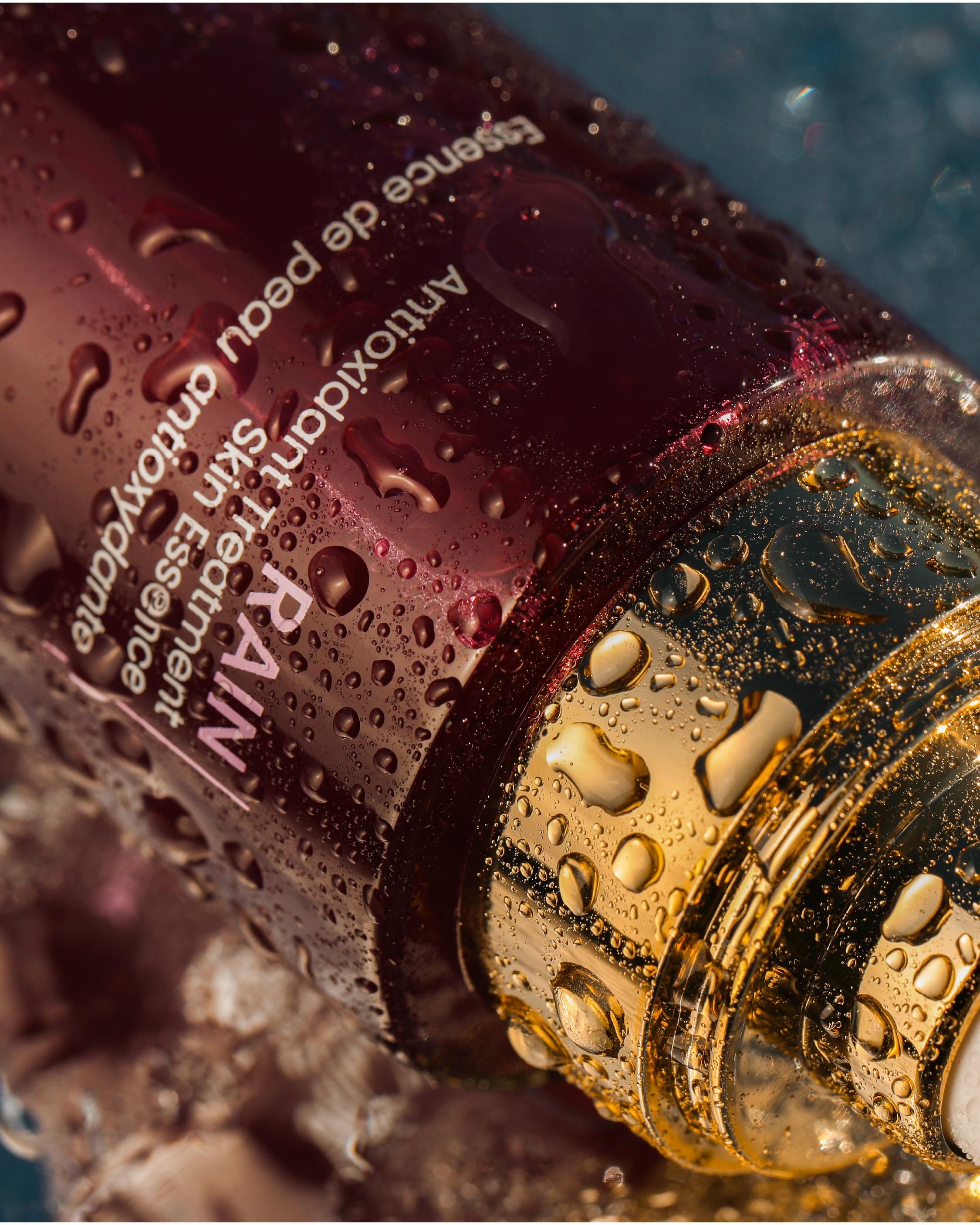 Close-up photograph of a bottle with water droplets on its surface, showing partially visible text in English, including the words 'Advance' and 'reduction'. The bottle appears to be made of glass with a gold-colored cap, and the background is out of focus with a blue hue.