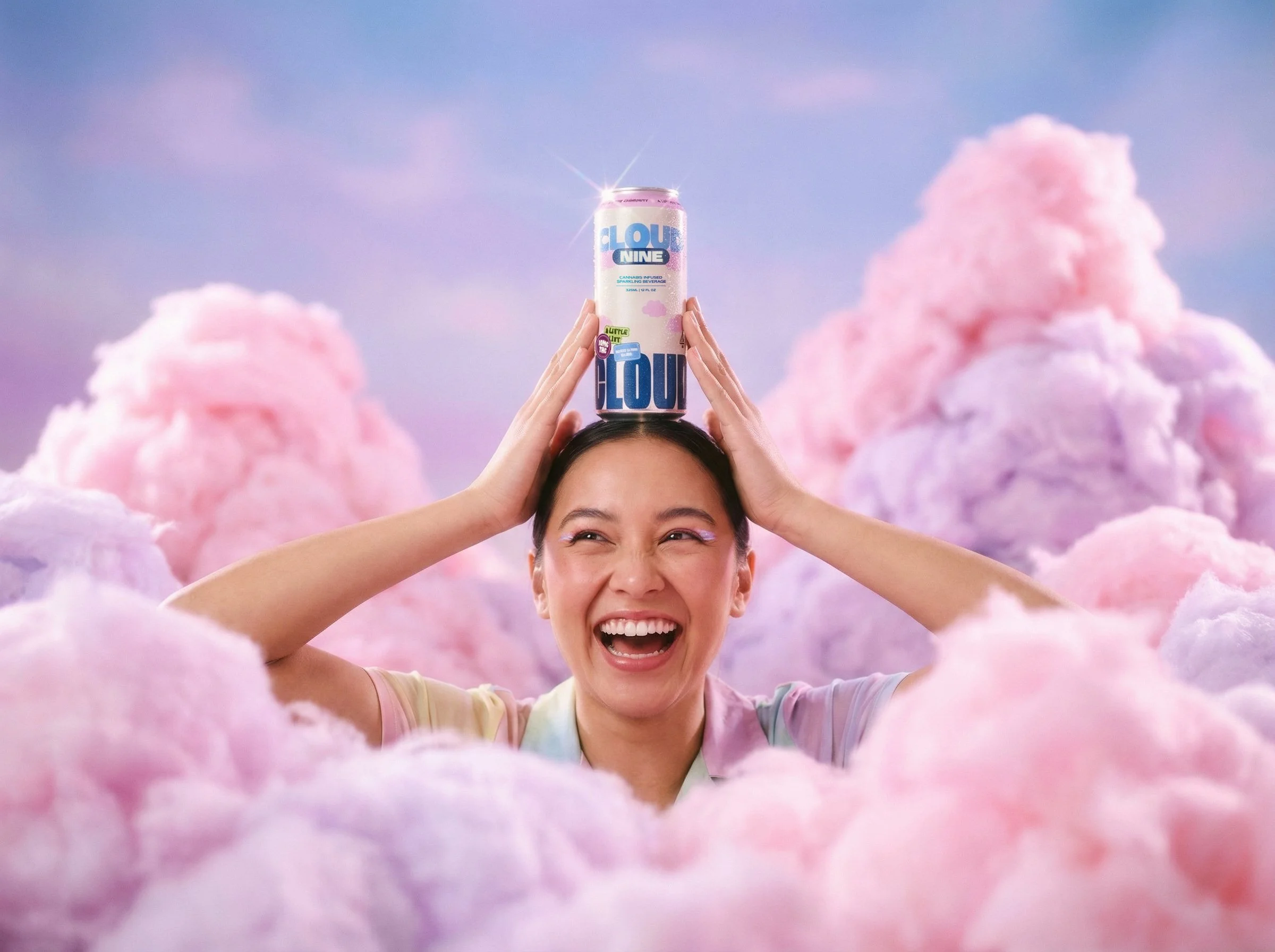 A woman holding a can of Cloud Nine cannabis-infused sparkling beverage on her head, smiling, with a colorful cotton candy cloud sky background.