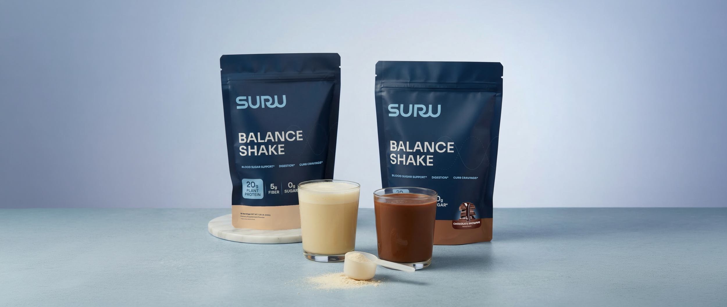 Two bags of SURU Balance Shake with glasses of prepared shakes, one vanilla and one chocolate, on a light blue surface with a small white spoon and powder.