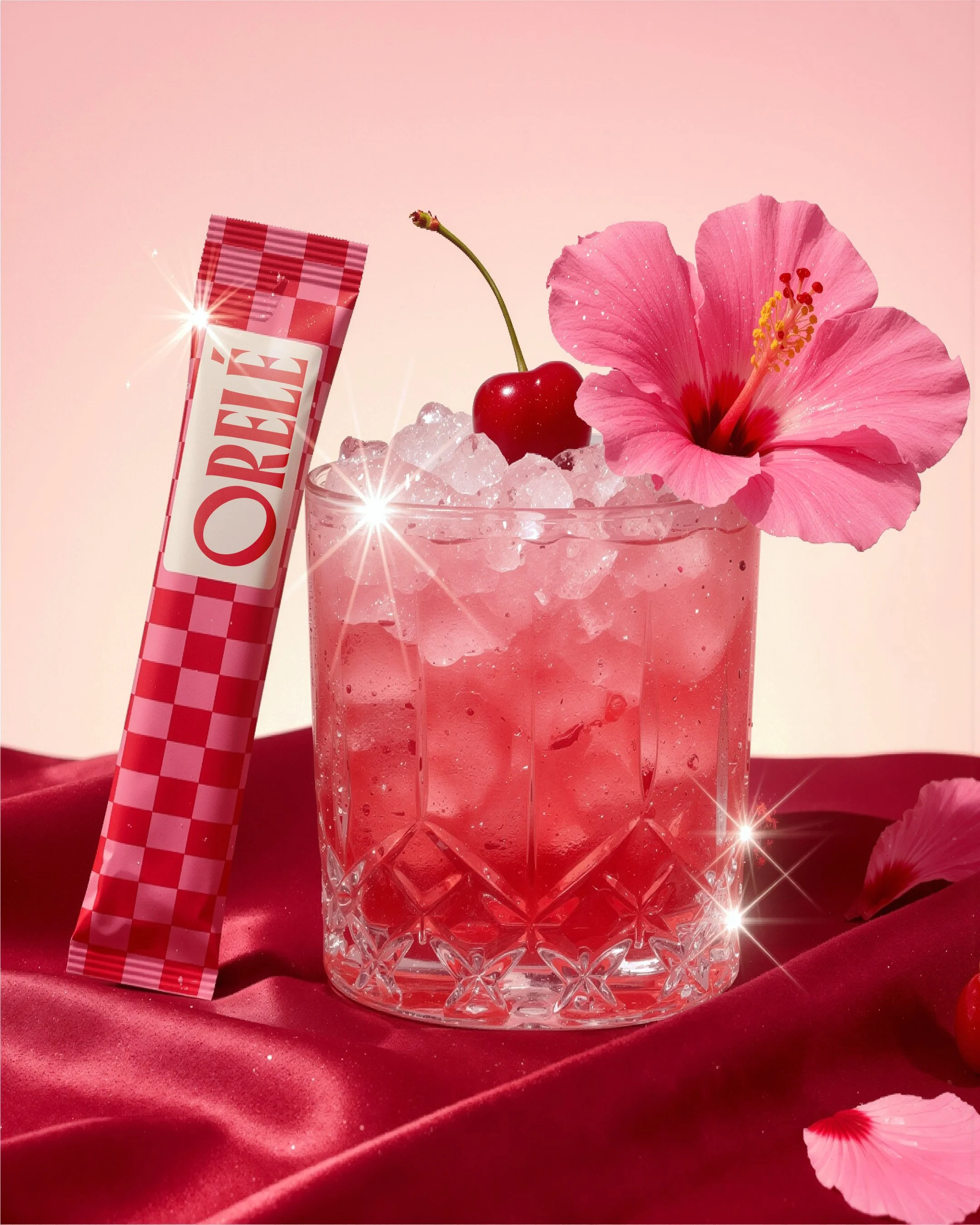 A pink tropical drink topped with crushed ice, garnished with a red cherry and a pink hibiscus flower, with a pink checkered straw, set on a red velvet cloth