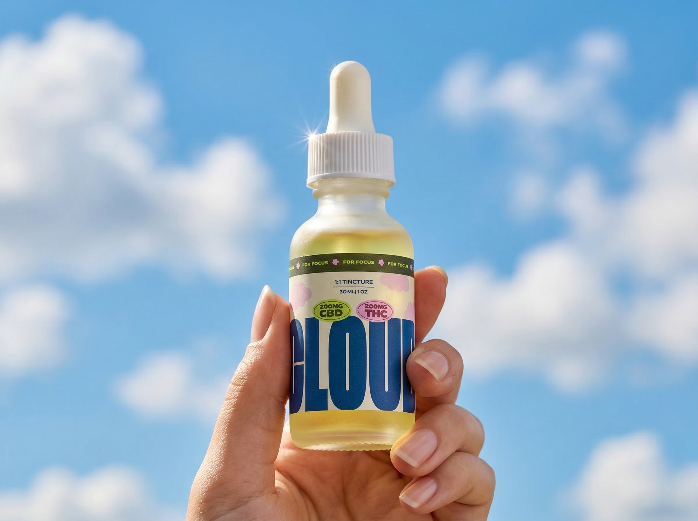 A hand holding a small bottle of CBD and THC tincture with a bright blue sky and some clouds in the background.