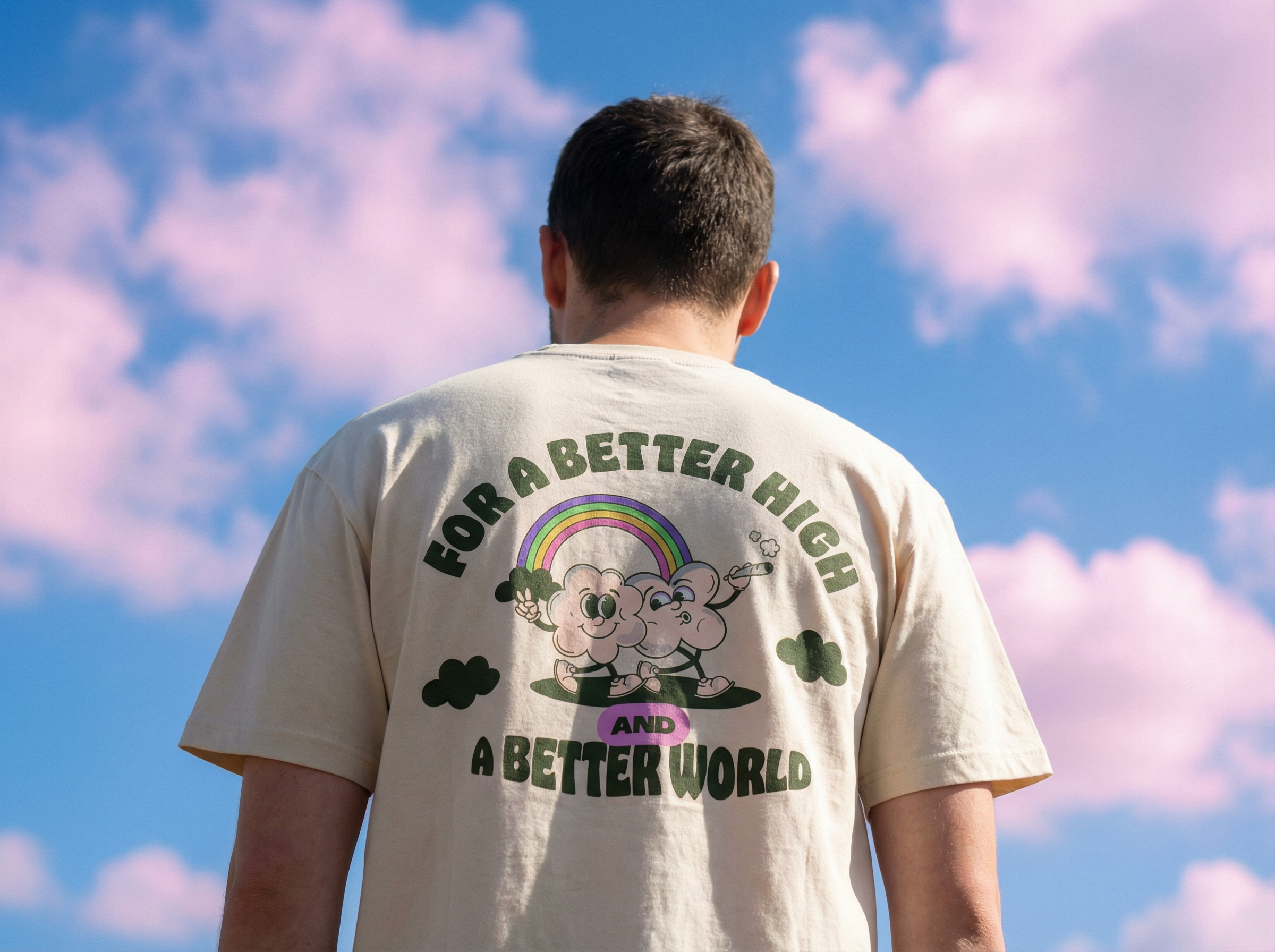 Back of a person wearing a beige t-shirt with a colorful cartoon cloud character and rainbow, text about a better world, standing outdoors under a sky with pink and blue clouds.