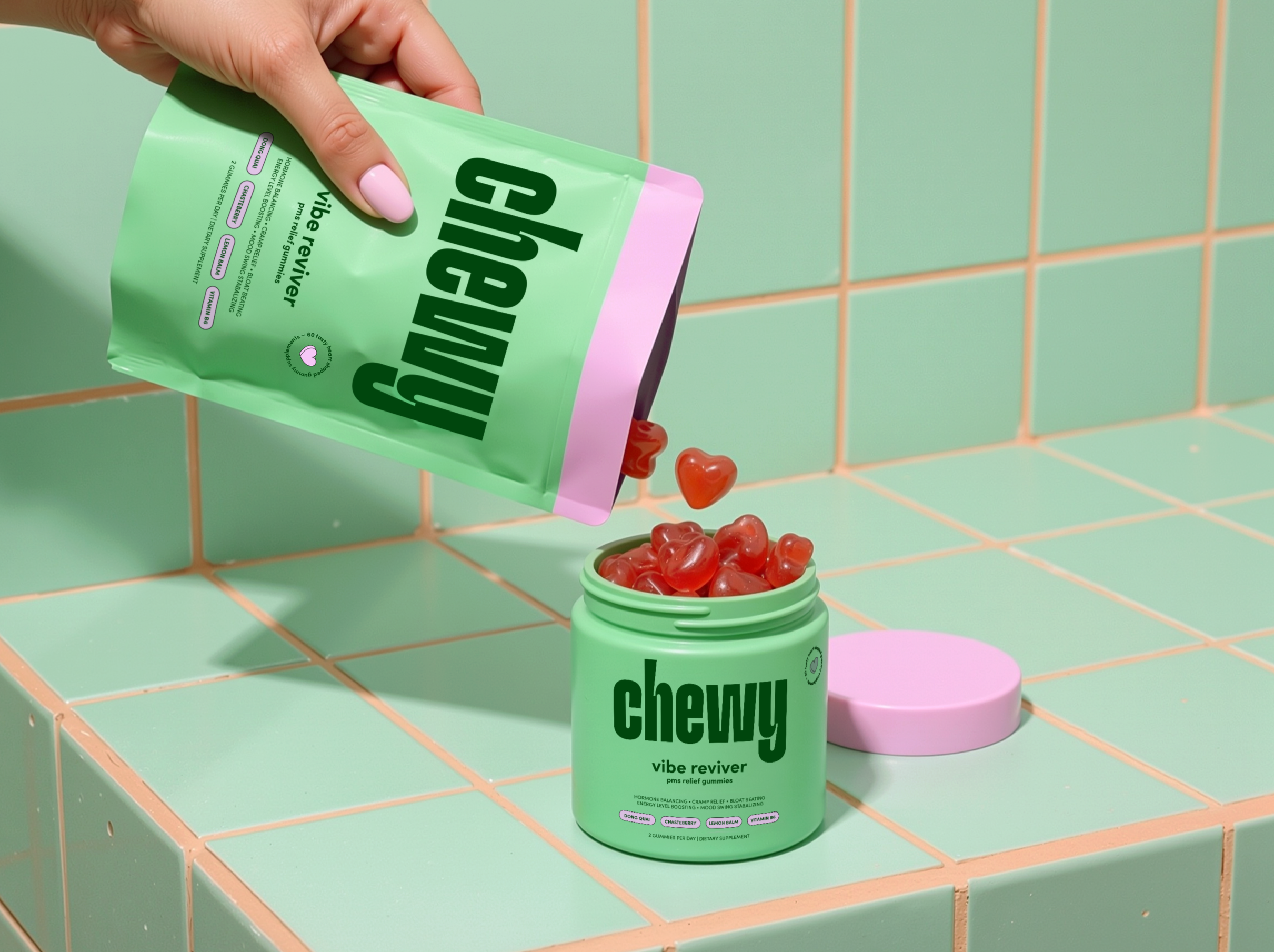 A hand with pink nail polish holding a green packet of Chewy vibe reviver gummies near a green container of gummies on a tiled bathroom wall.