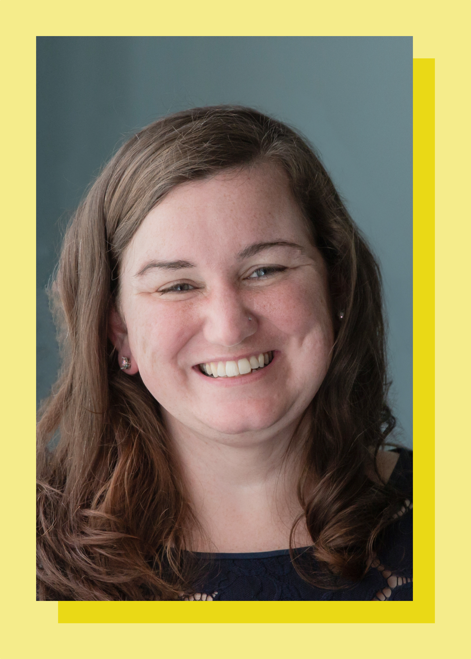 Smiling woman with brown hair wearing a dark top, against a blue background.