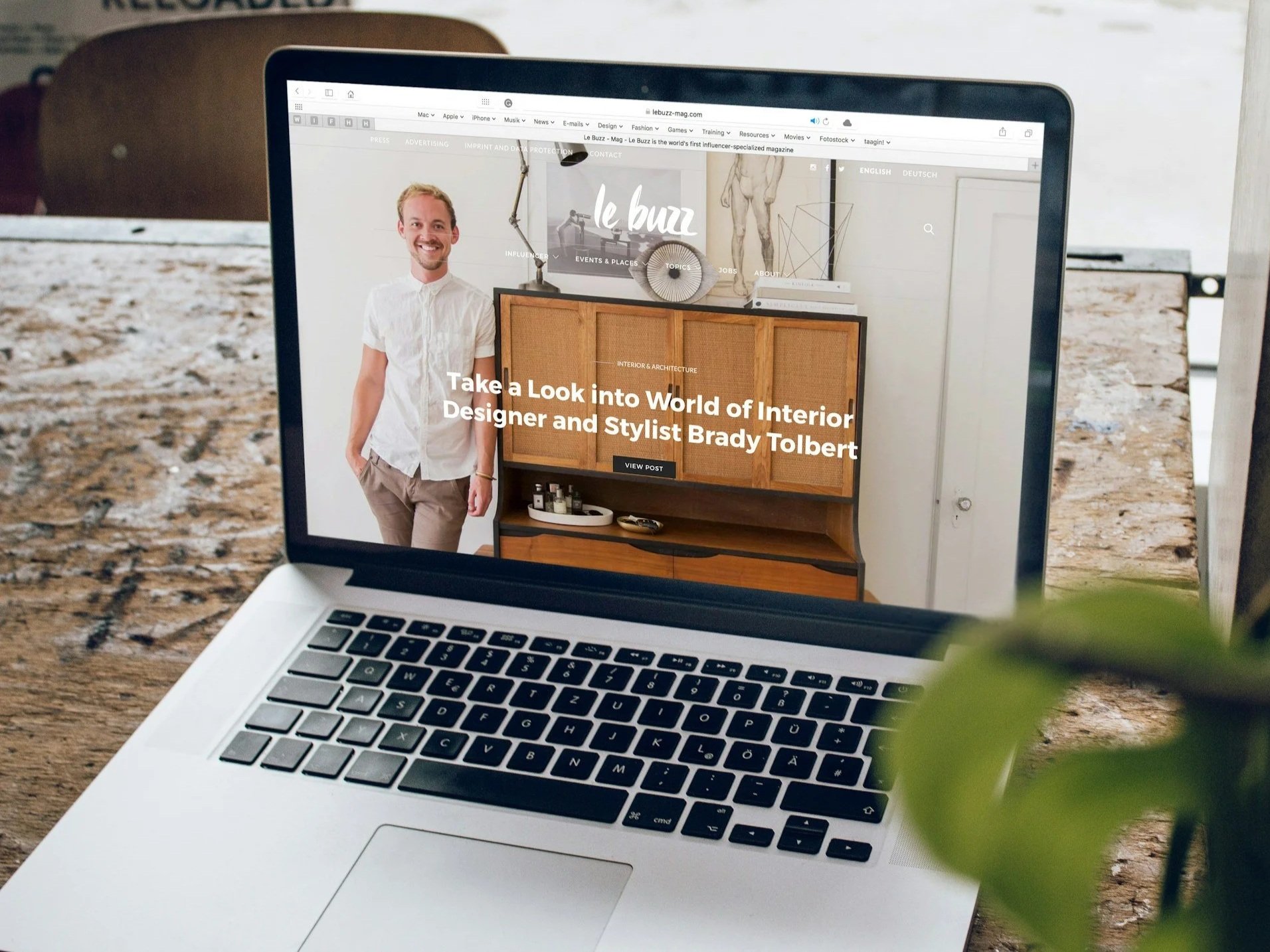 A MacBook laptop on a wooden table shows a webpage about interior design.