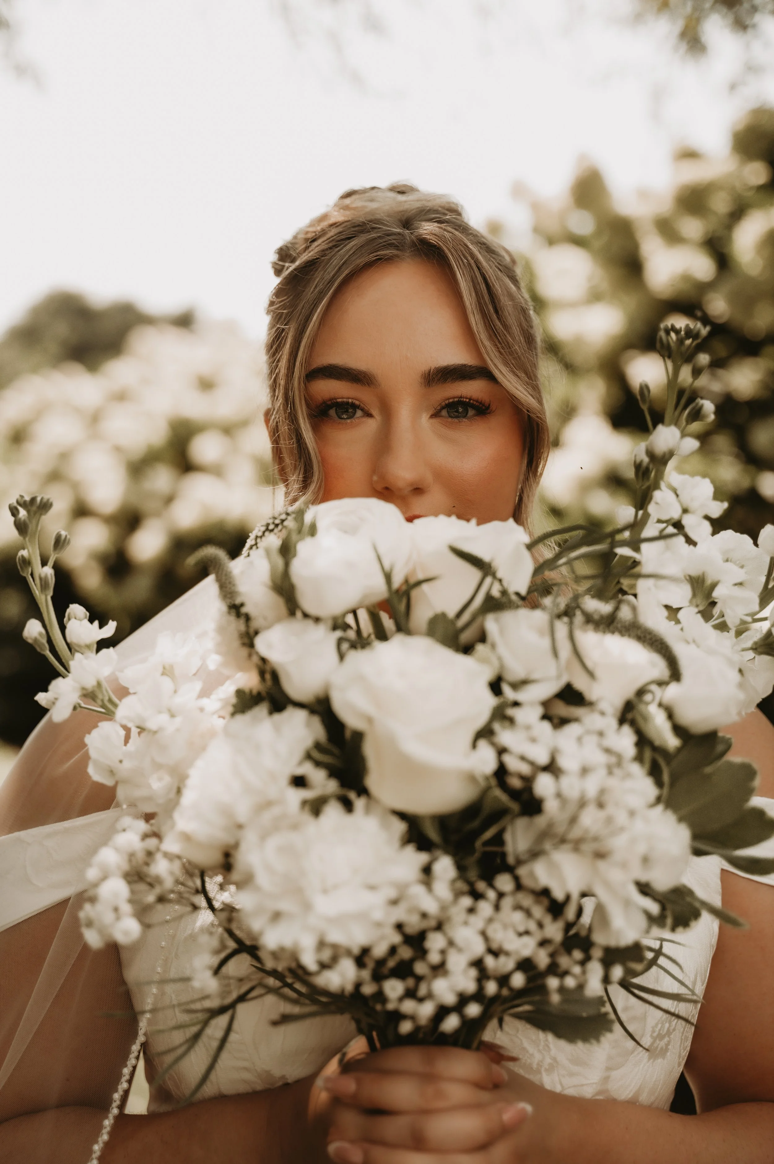 A woman holding a large bouquet of white flowers, with a blurred outdoor background.