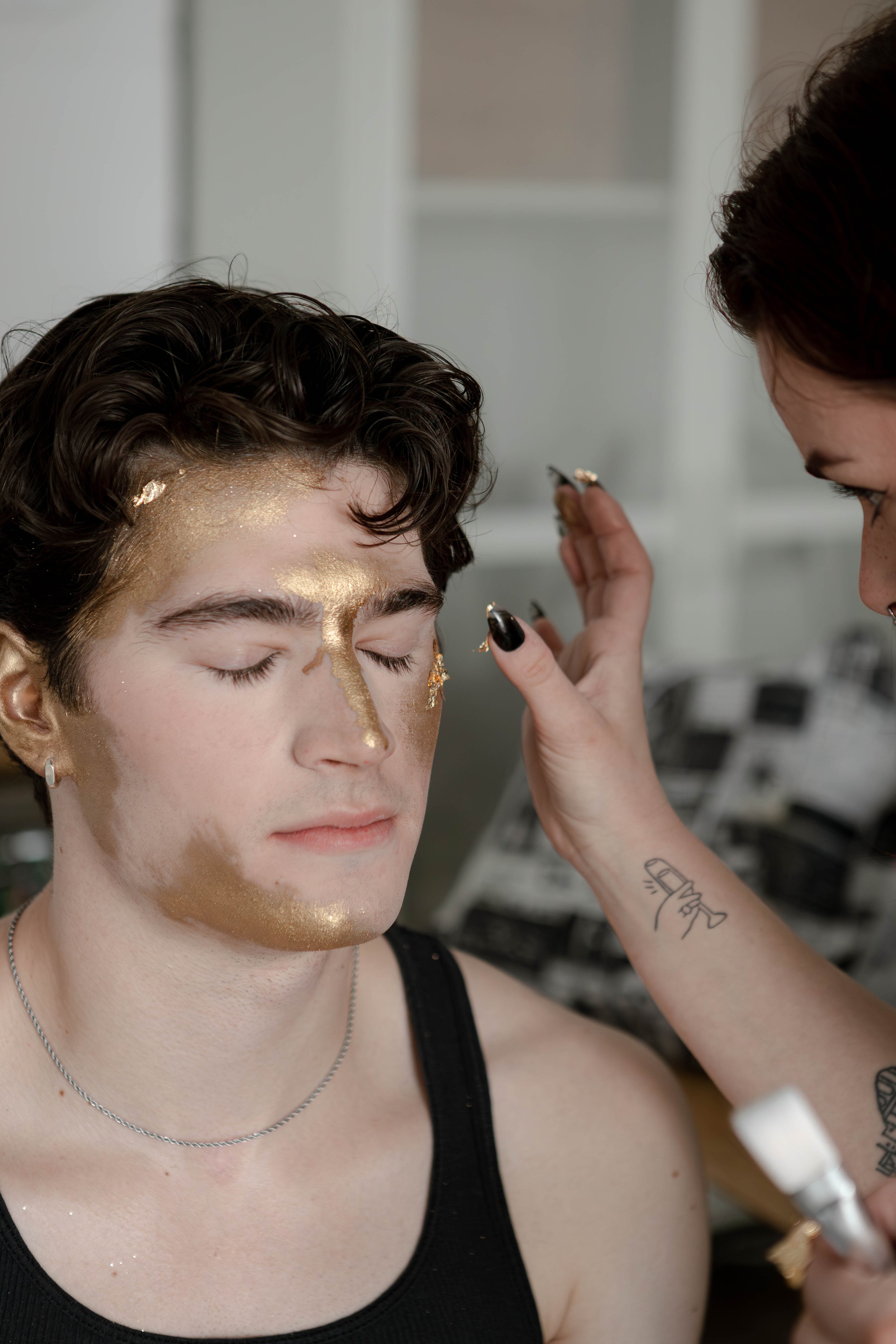 Person with closed eyes having gold makeup applied on their face during a makeup application session.