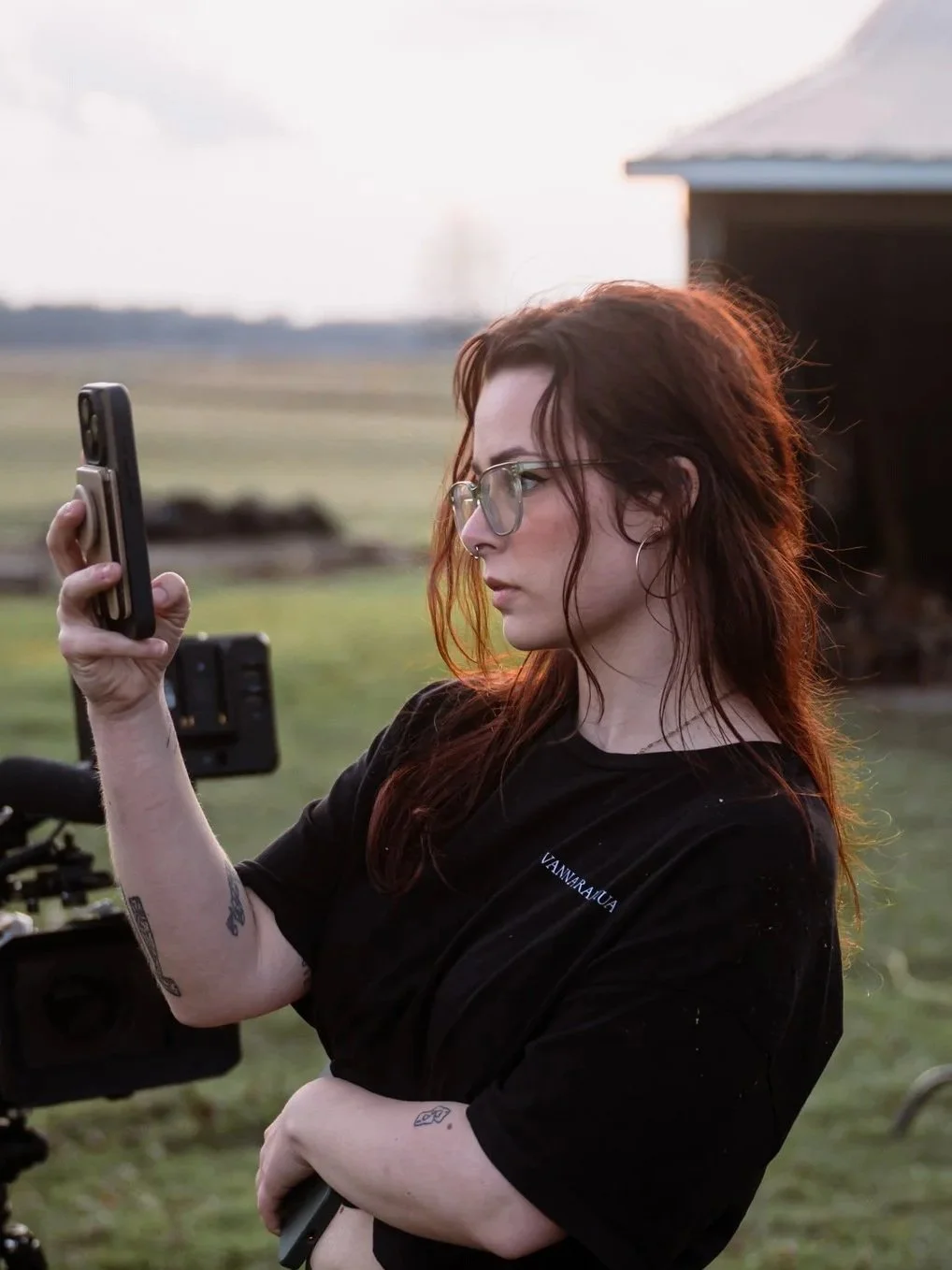 A woman with red hair and glasses taking a selfie outdoors during sunset