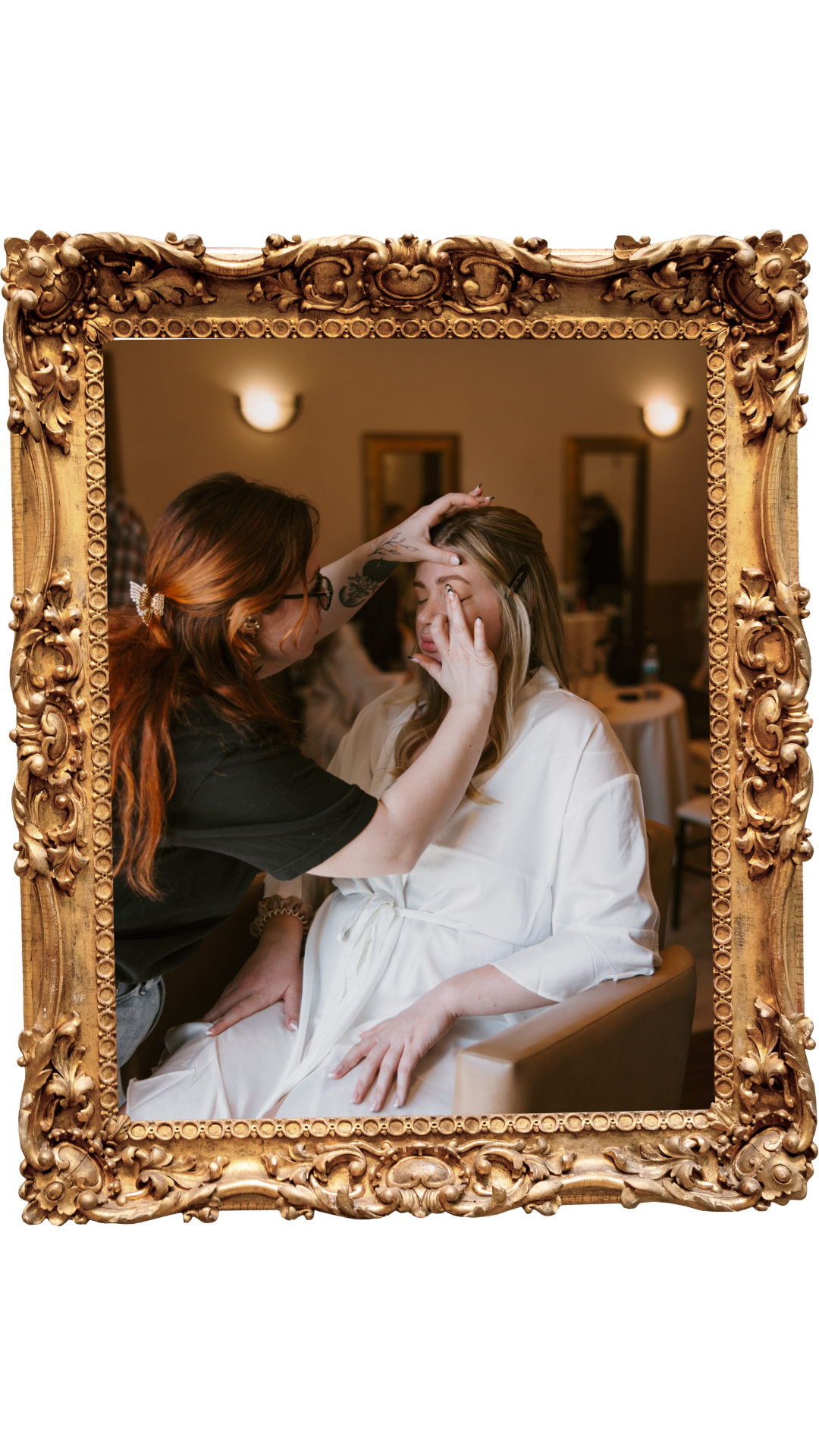 A makeup artist applies makeup to a woman sitting in front of a mirror with a detailed gold ornate frame.