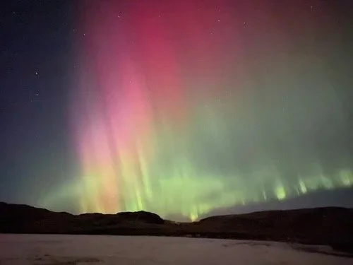 Northern lights in the night sky over a dark landscape.