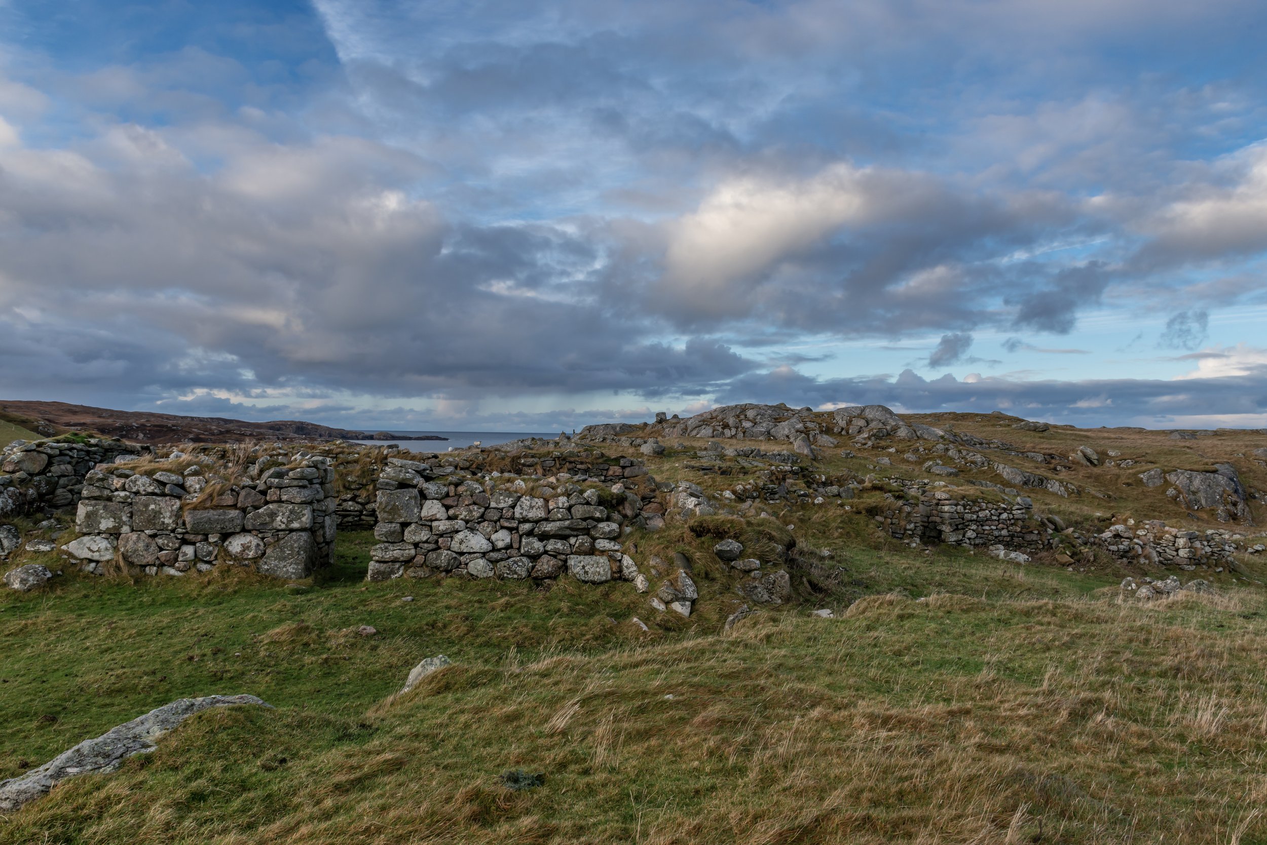 Scenic view of an open landscape with ancient stone ruins surrounded by grassy hills under a partly cloudy sky.