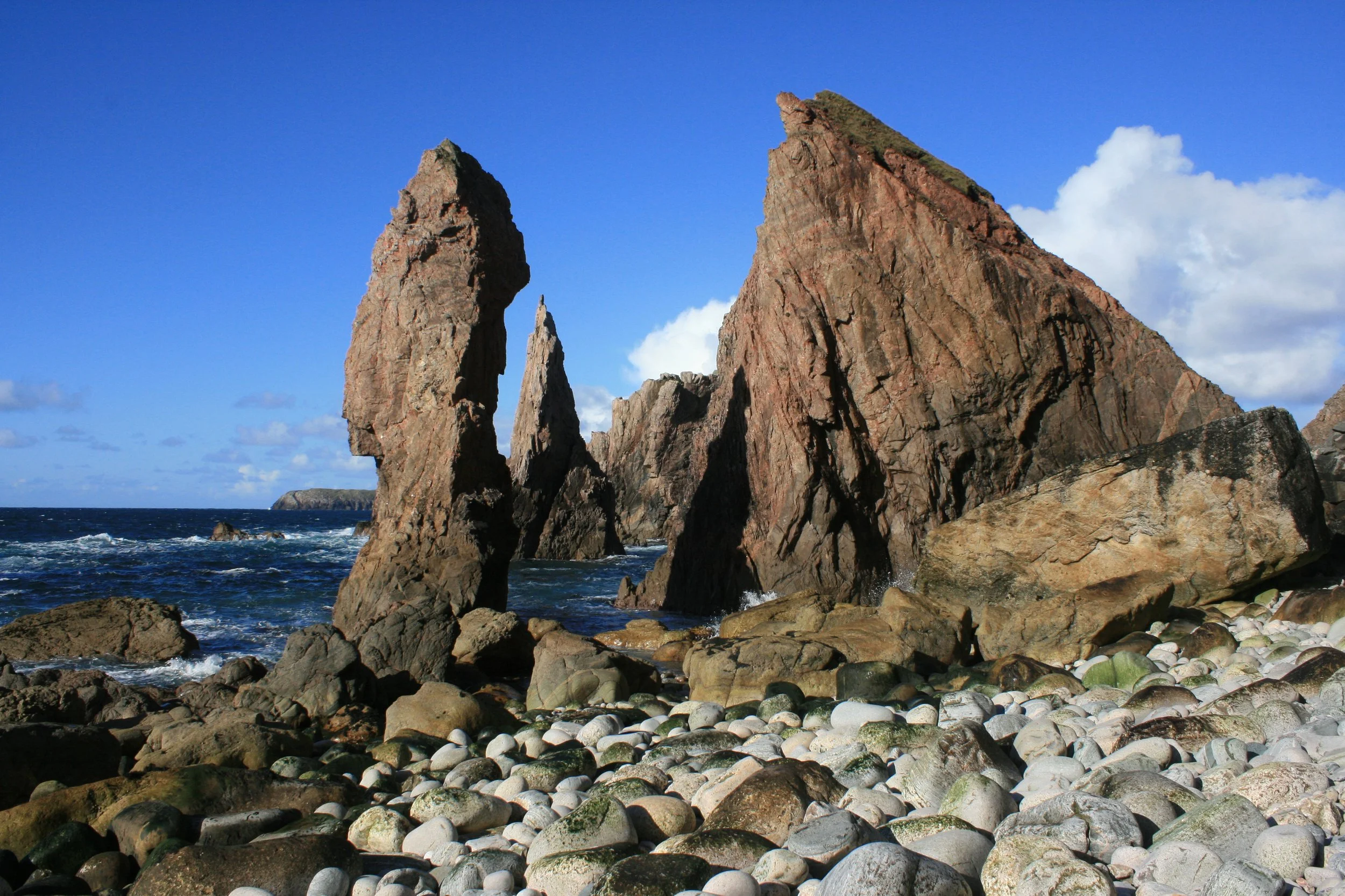 Rugged sea stack formations along a rocky shoreline under a partly cloudy sky.