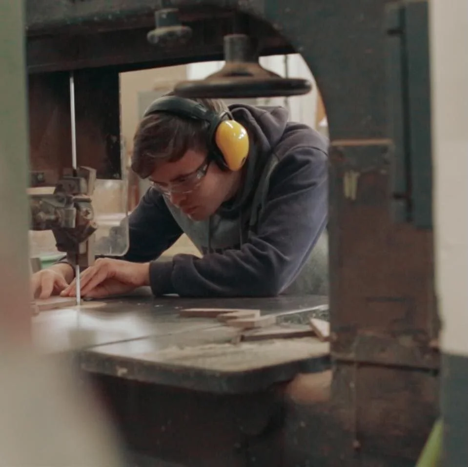 A person wearing safety ear protection and glasses is working on a woodworking project in a workshop.
