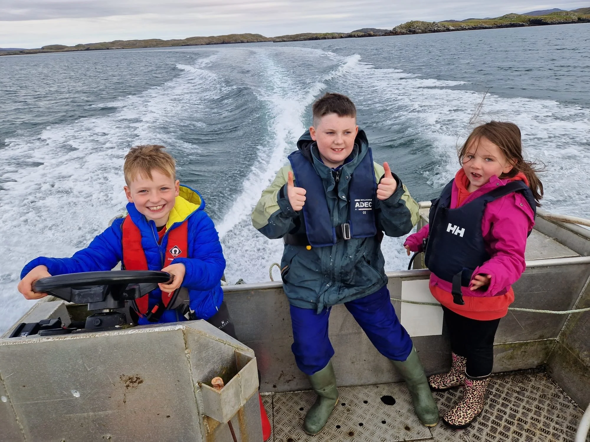 3 children with lifejackets on boat out at sea. Uig Community.
