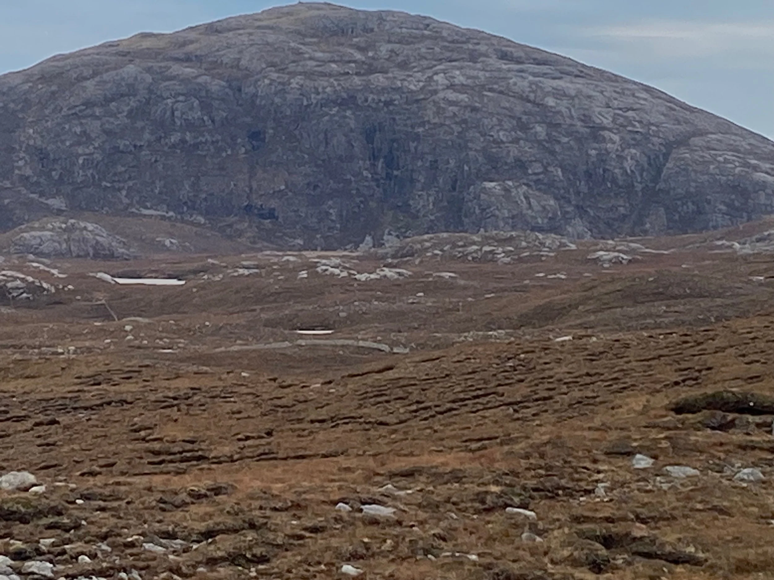 A large rocky mountain in the background with sparse brown terrain and patches of snow in the foreground.