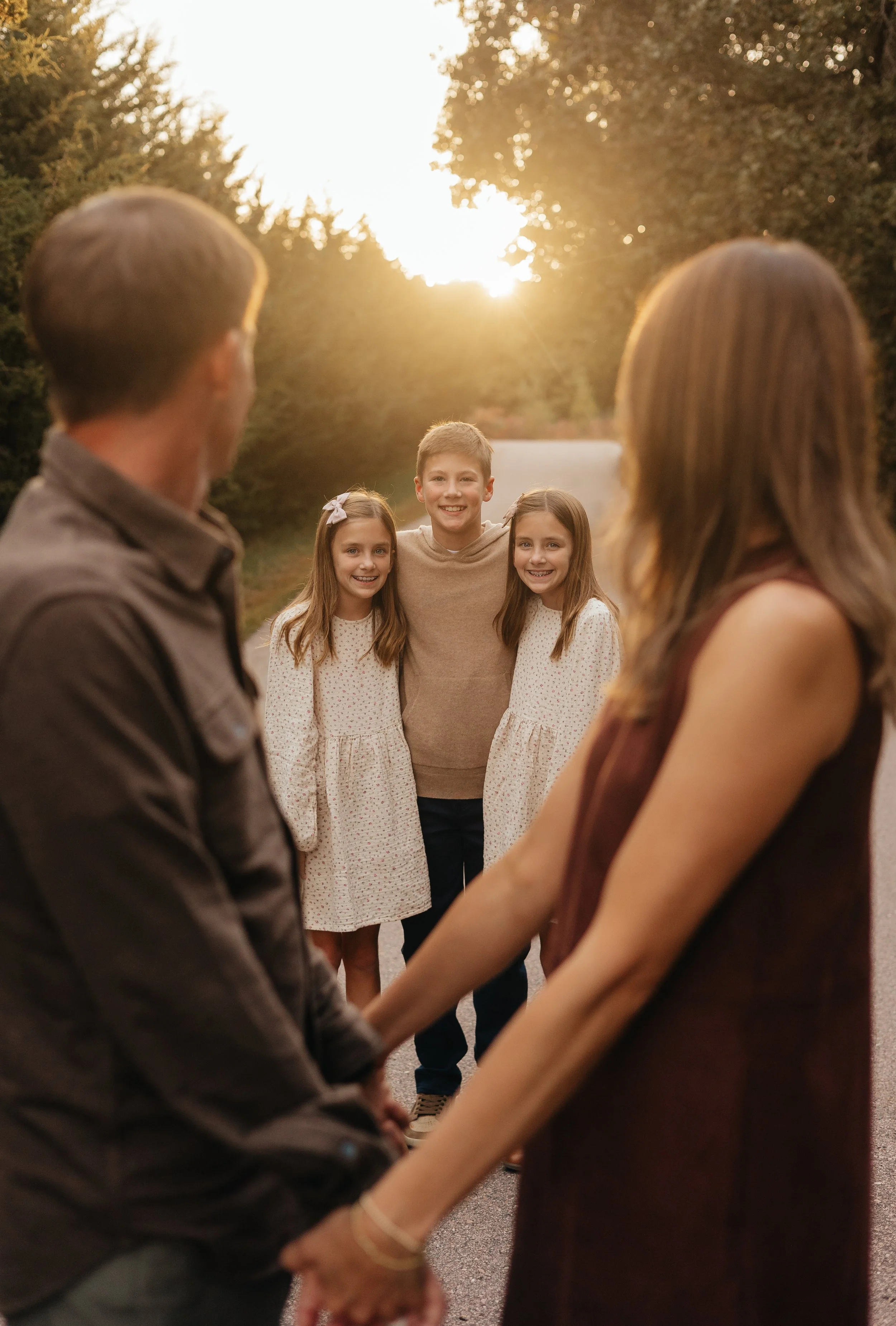 A family standing outside at sunset, holding hands, with children smiling in the background.