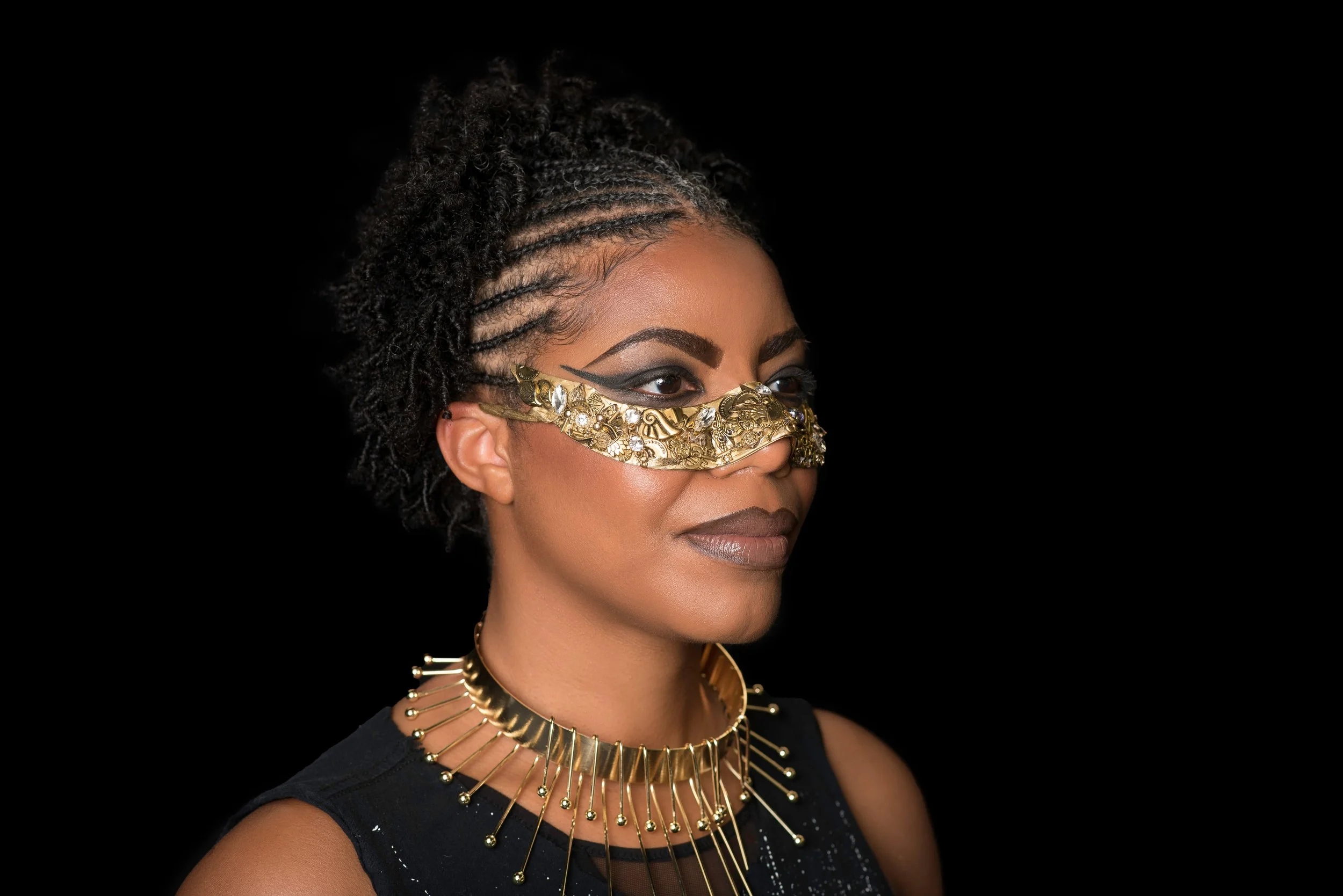 Artistic close-up of a woman with braided hair wearing an ornate gold mask and choker, showcasing high-fashion natural hair artistry.