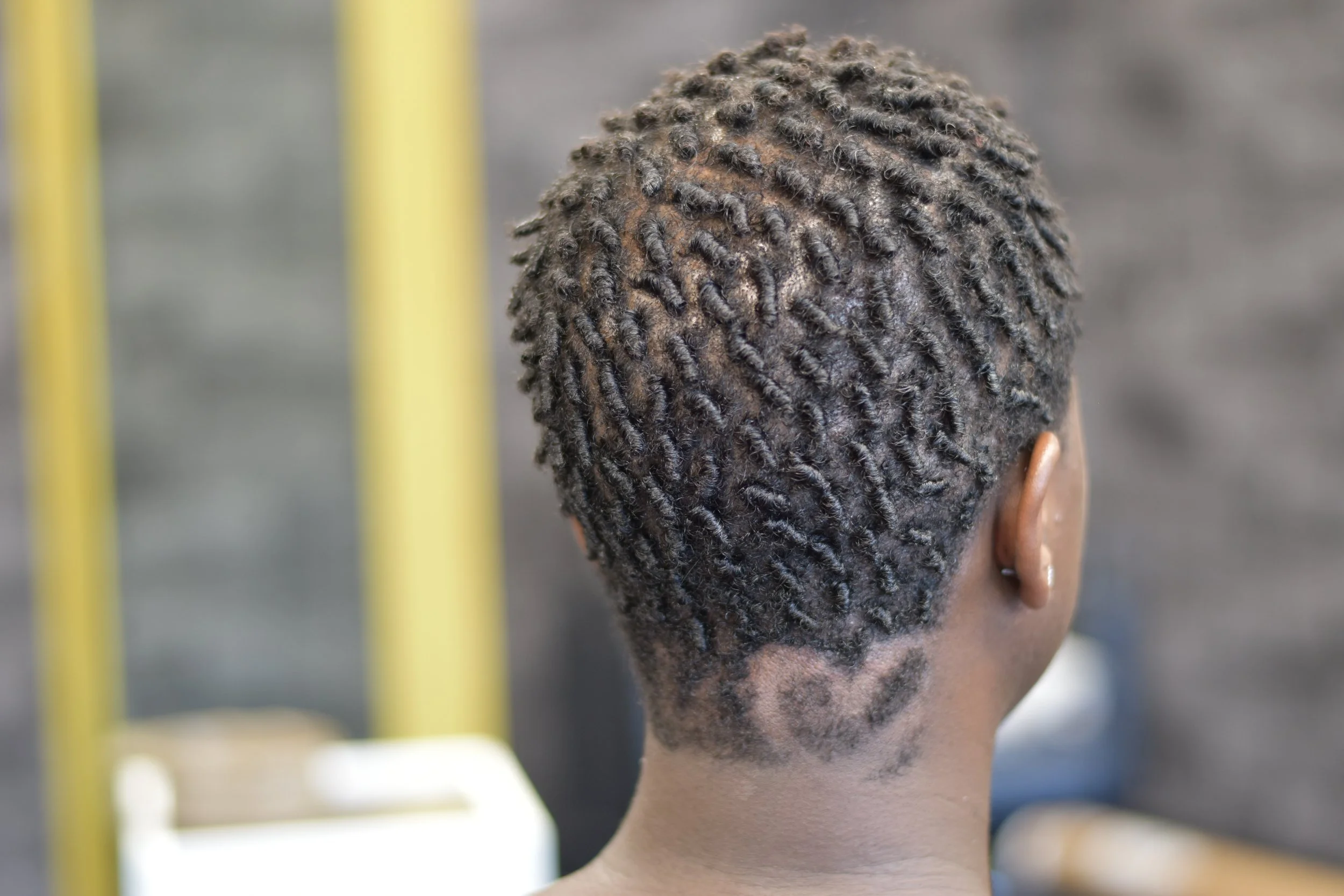 Back view of a professional tapered fade on natural hair with a custom geometric shaved design at the nape, styled at Mr. Naturalz Salon.