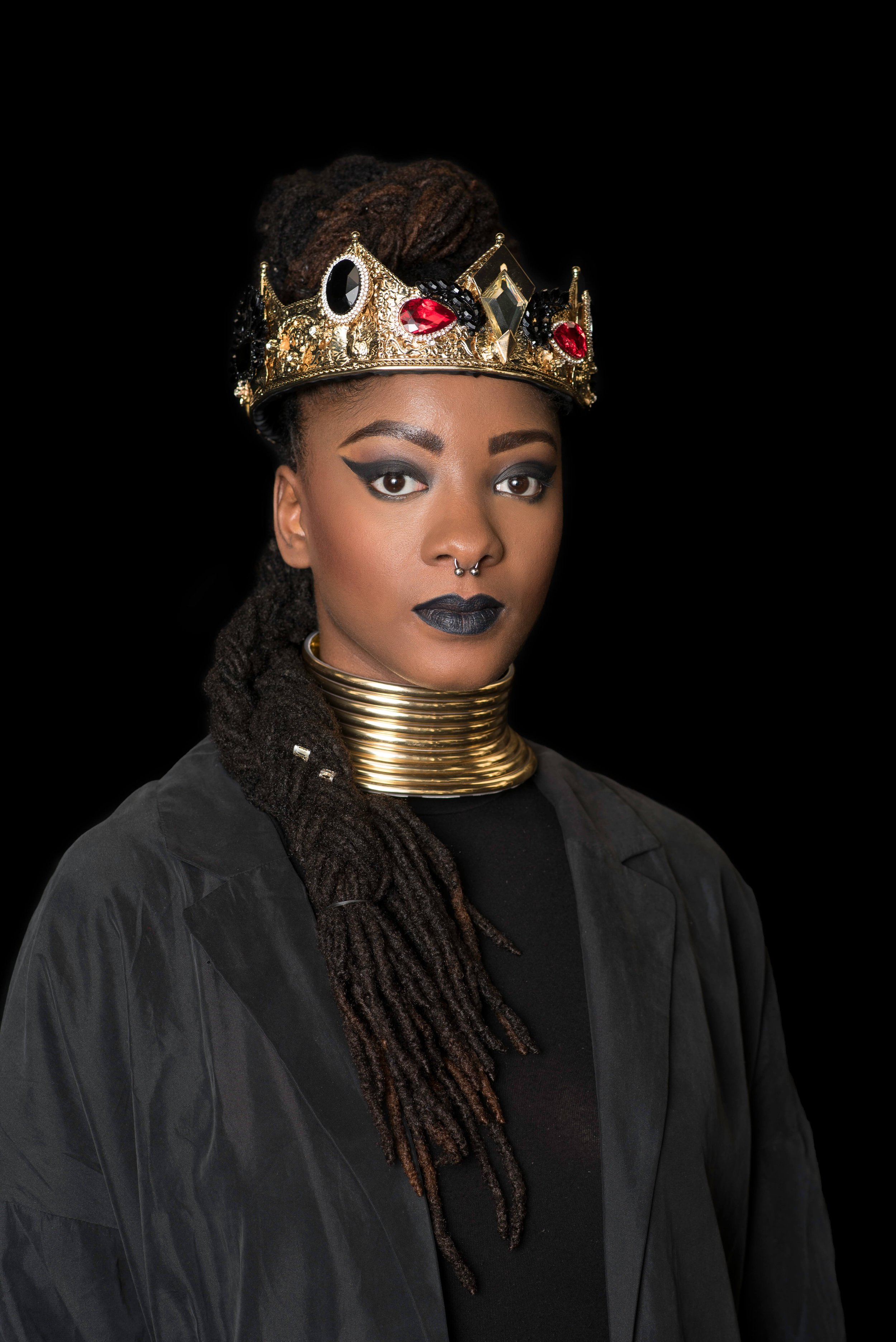 Regal portrait of a woman with long locs wearing a gold jeweled crown and traditional neck rings, representing the "High-Vibe" energy of Mr. Naturalz Salon.
