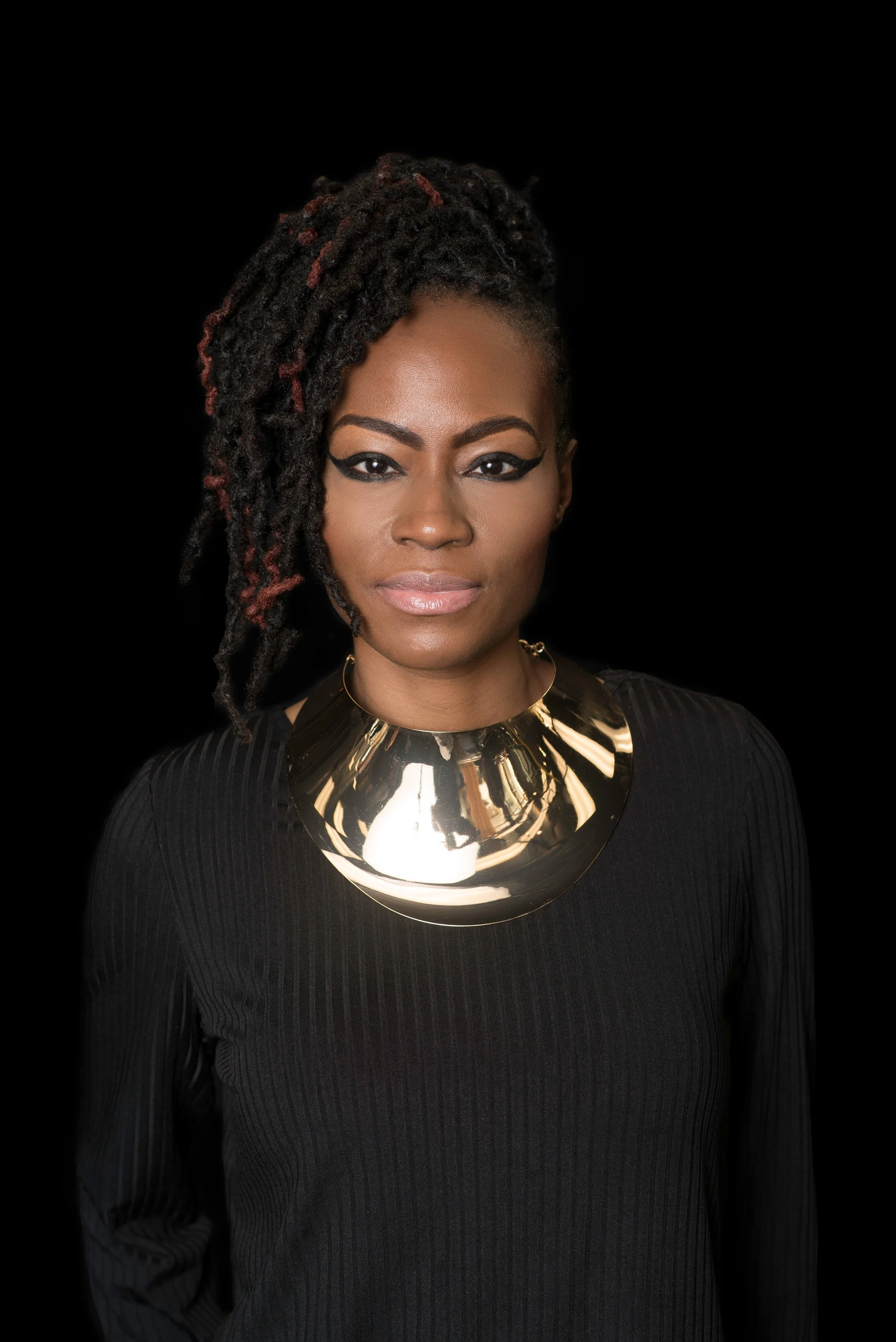 Professional portrait of a woman with textured locs and a statement metallic necklace against a dark background, highlighting natural beauty and loc maintenance.