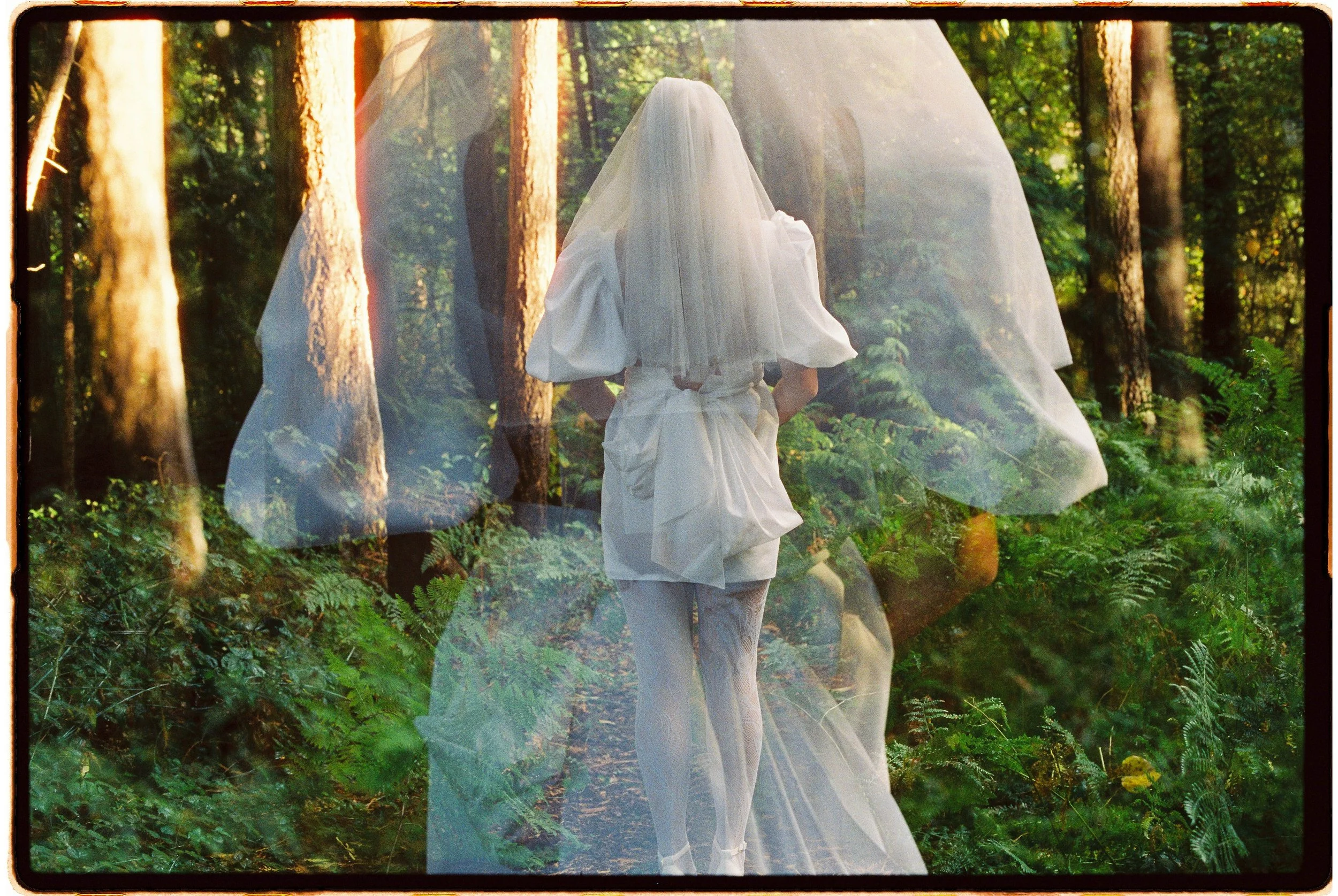 Double exposure photo of a woman in a white dress and veil standing in a forest with sunlight filtering through trees, combined with a sheer fabric overlay.