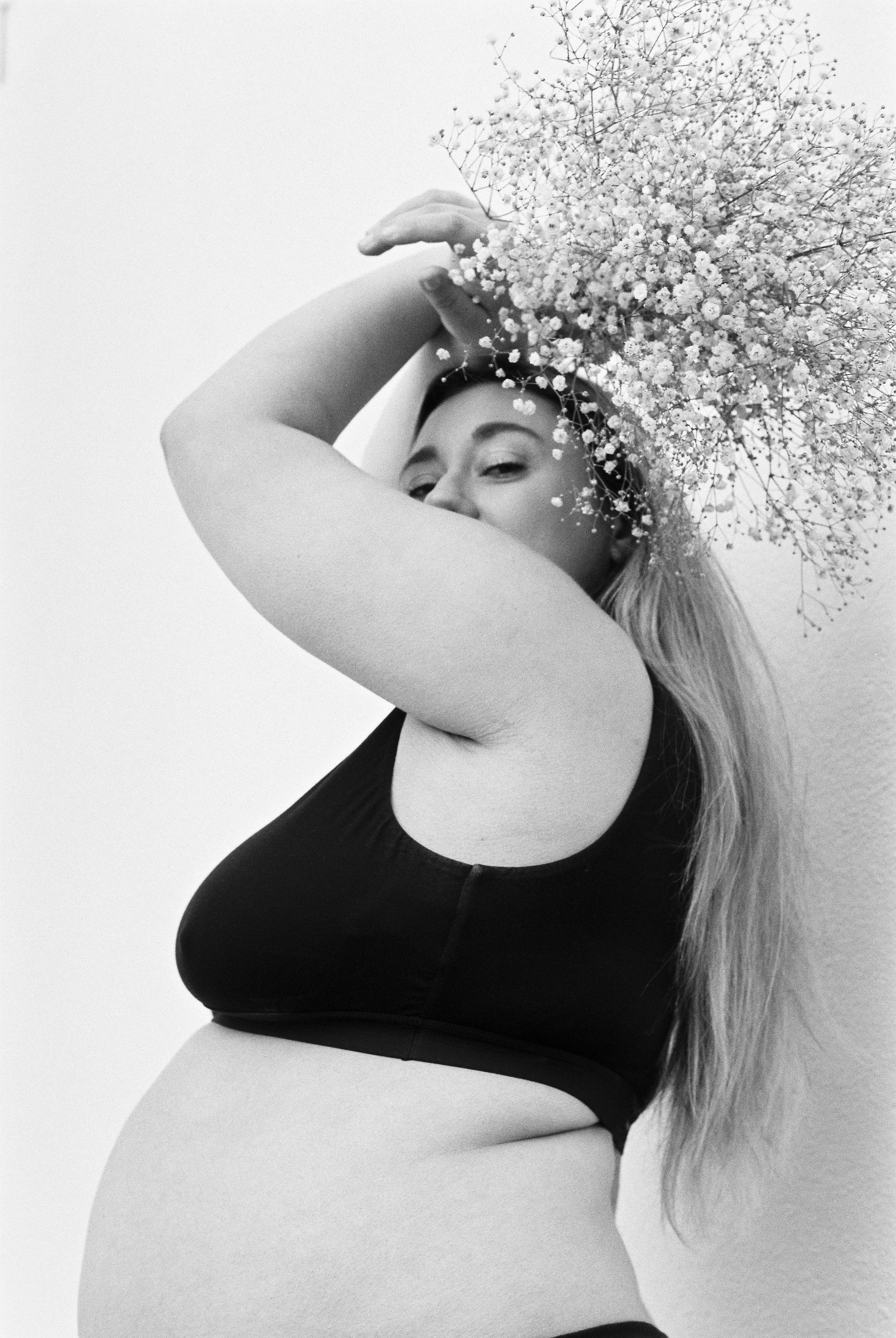 A woman with long hair holding a bouquet of baby's breath flowers over her head, partially covering her face, in a black and white photo.