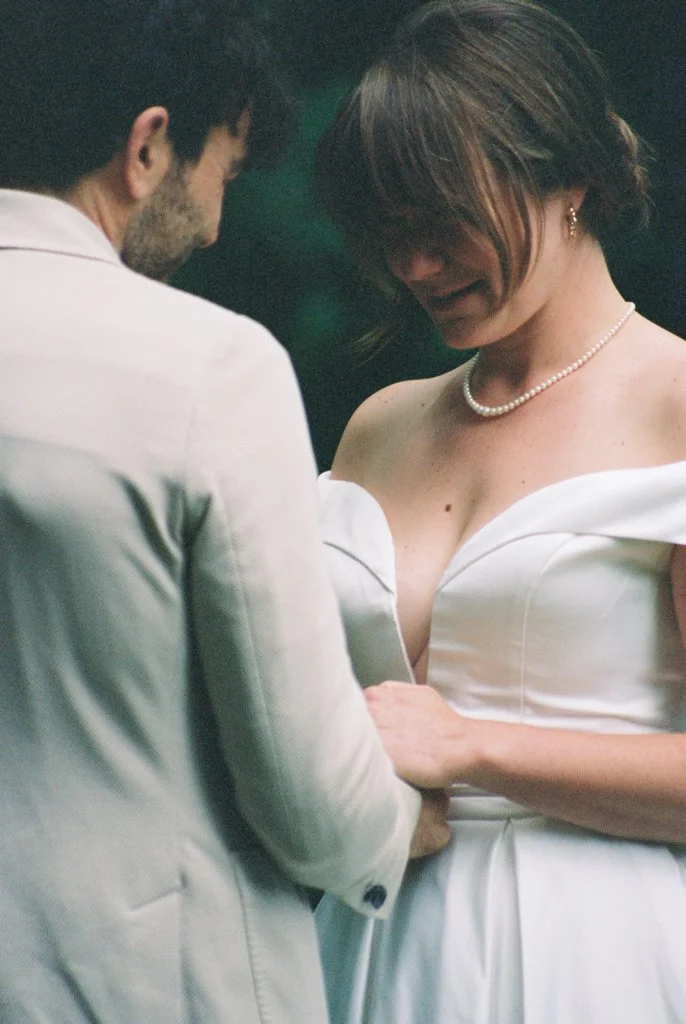 A woman and man in wedding attire sharing an intimate moment, with the woman holding the man's hand and they are looking at each other.