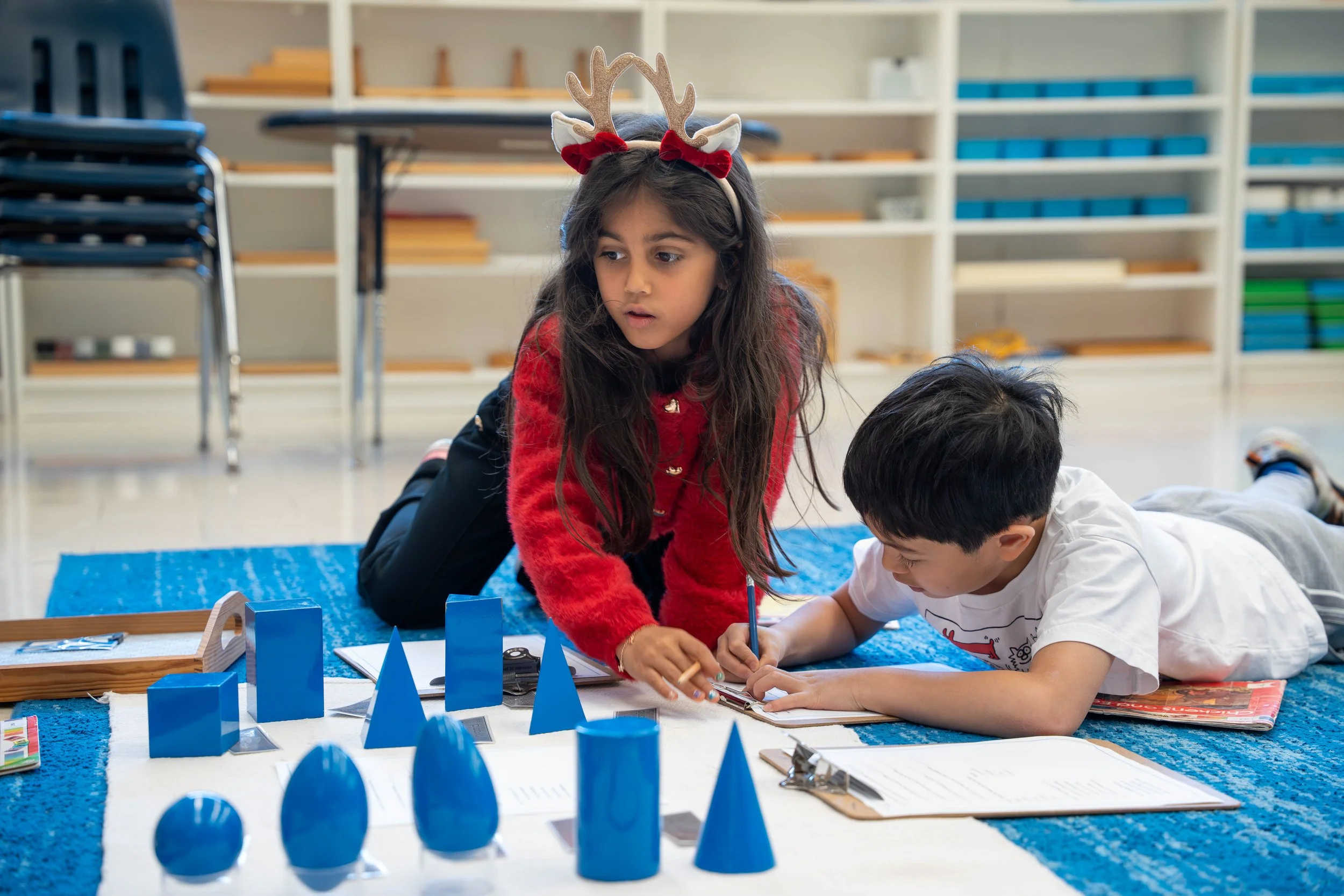 Two Montessori students at Bannockburn Independent school working on a project with blue geometric shapes and papers.