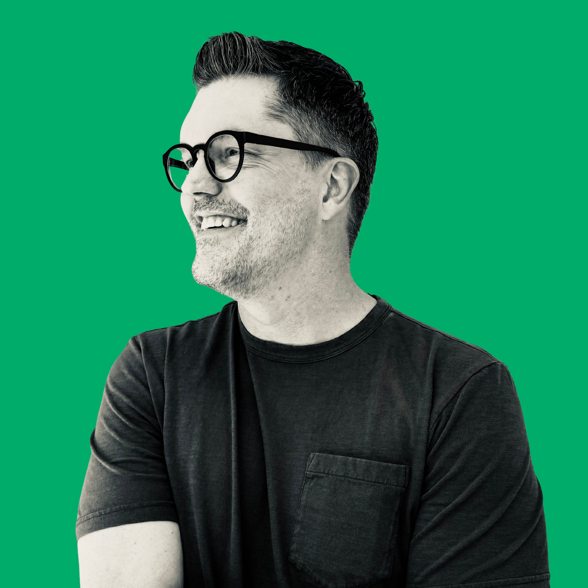 A smiling man with glasses and gray hair, wearing a black t-shirt, against a green background.