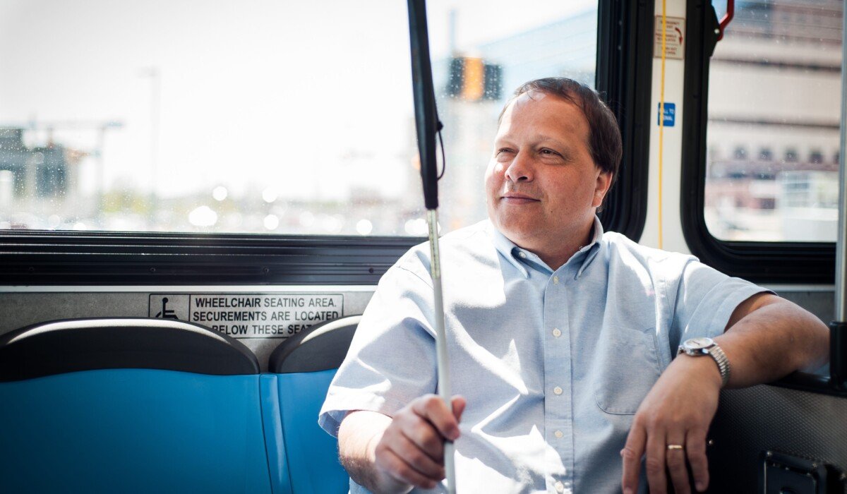 A person sitting on the bus, holding a white cane.
