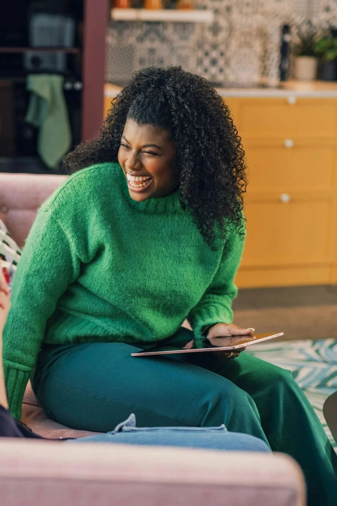 Woman laughing while using a tablet in a comfortable setting.