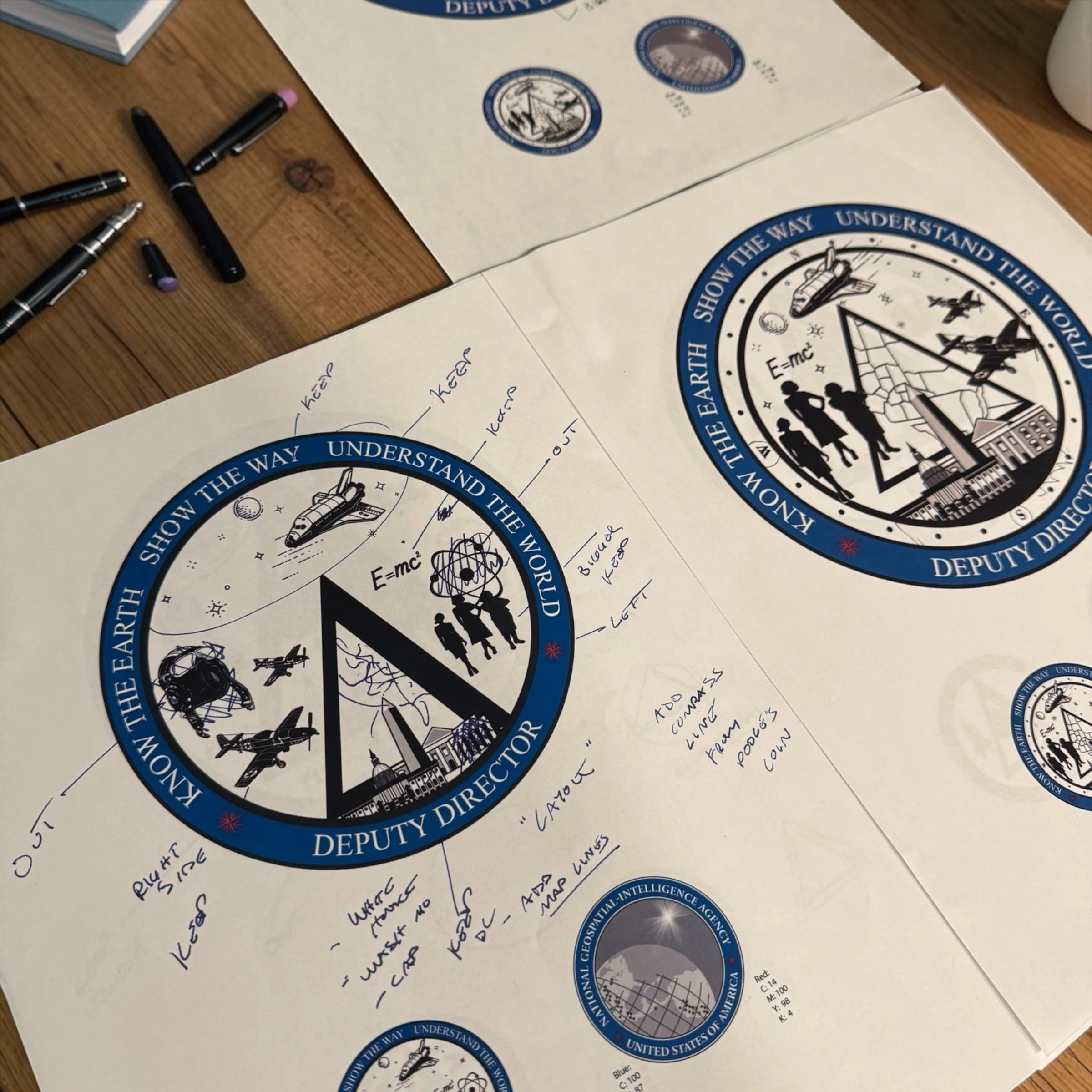 Designs for the Deputy Director of the National Geospatial-Intelligence Agency, with notes on various elements like spacecraft, airplanes, and science symbols. The badge features a circular border with the inscription 'Show the Earth, Understand the World,' and contains illustrations of space, aircraft, and people, along with handwritten annotations.