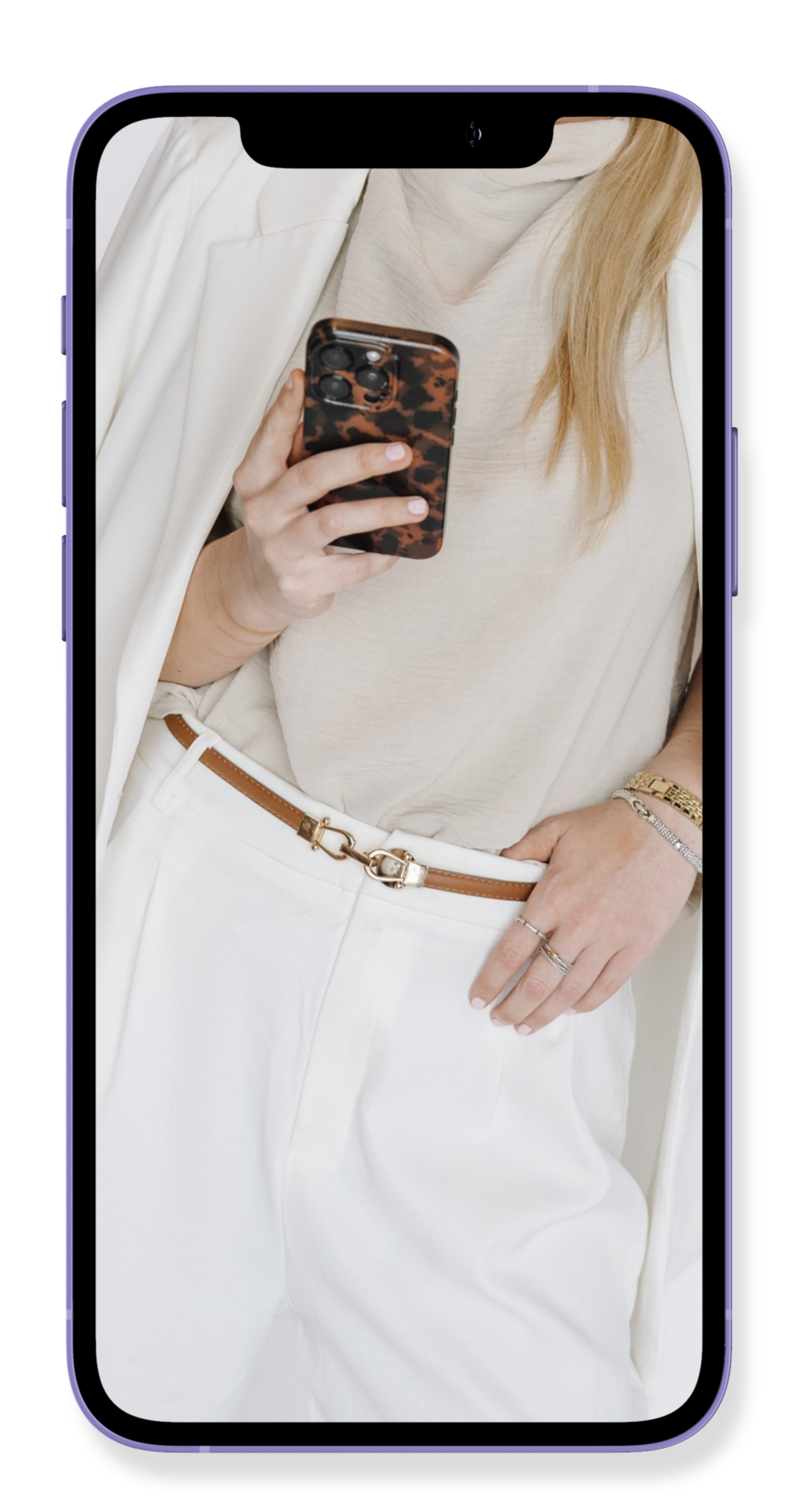 Close-up of a woman wearing white pants, a beige shirt, a white blazer, and accessorized with jewelry, taking a selfie with a smartphone that has a tortoiseshell case.