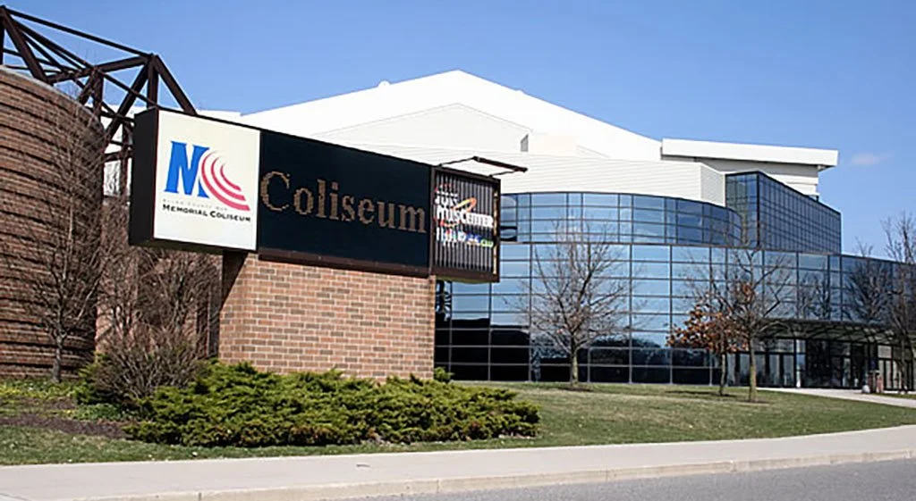 Exterior of the National Collegiate Memorial Coliseum with a brick and glass facade, trees, and a sign reading 'Coliseum.'