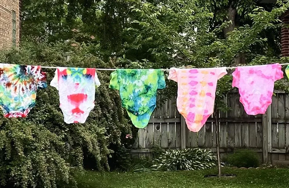 A clothesline with colorful, tie-dye underwear hanging outdoors in a backyard with green trees and a wooden fence.
