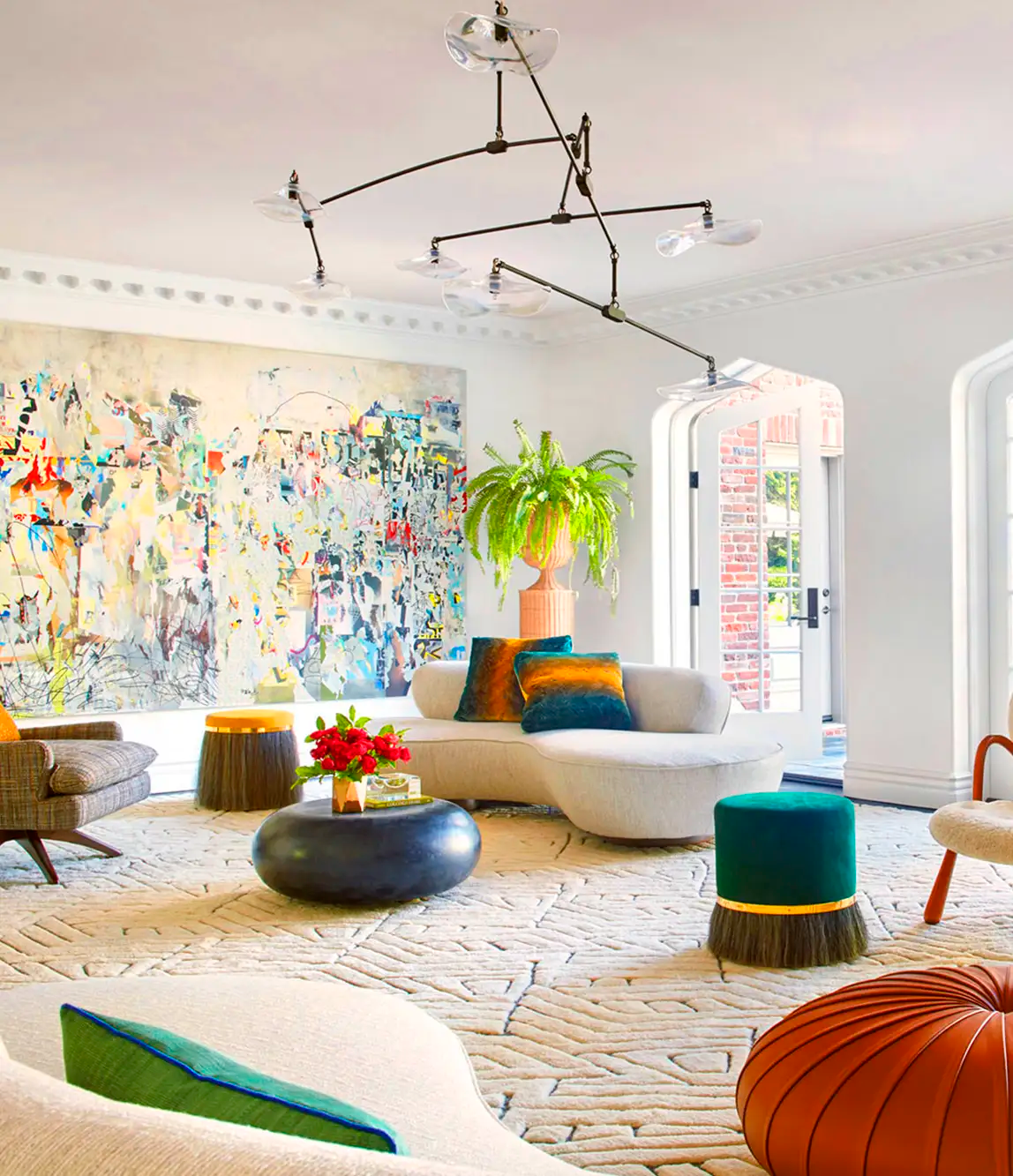 Bright living room with modern furniture, large colorful abstract artwork, green plant on a pink pot, and various colorful stools and cushions.