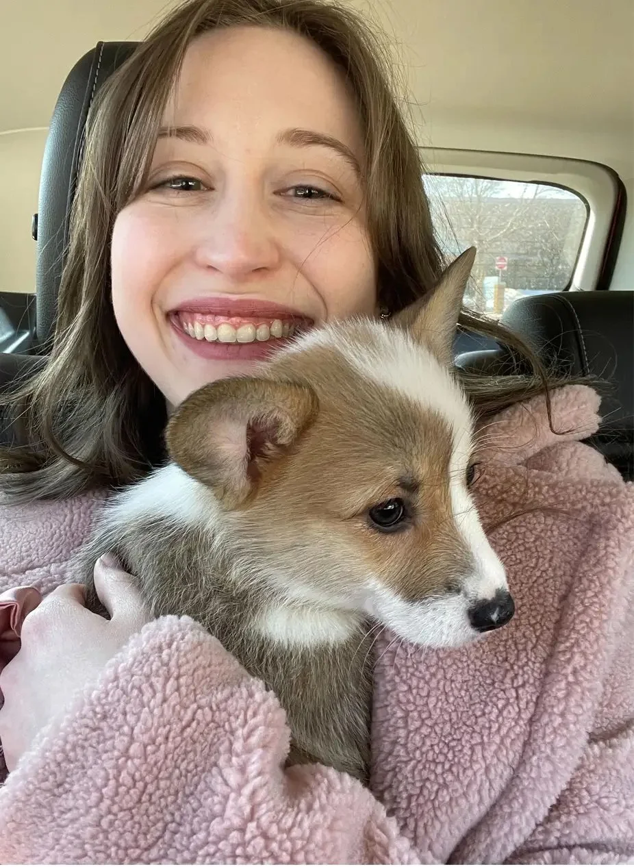 A woman smiling while holding a small puppy inside a vehicle.