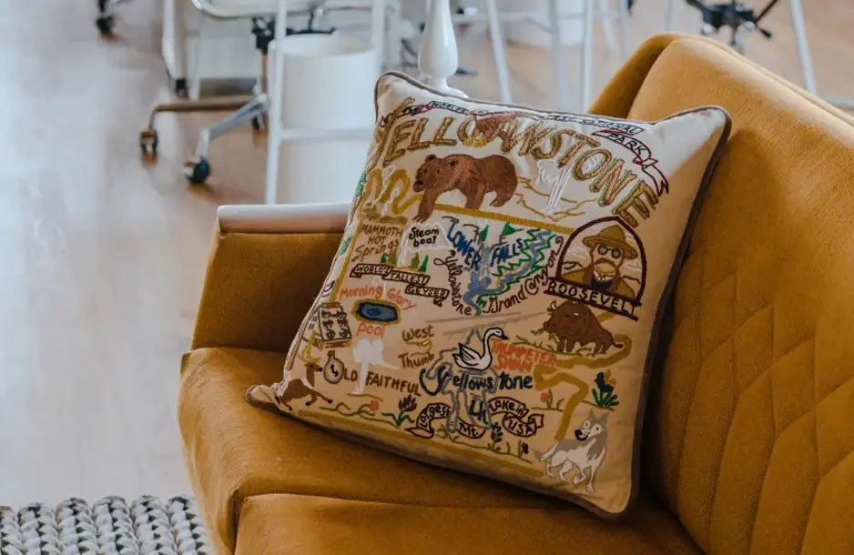Decorative pillow with an embroidered map of Yellowstone National Park on a mustard-colored sofa.