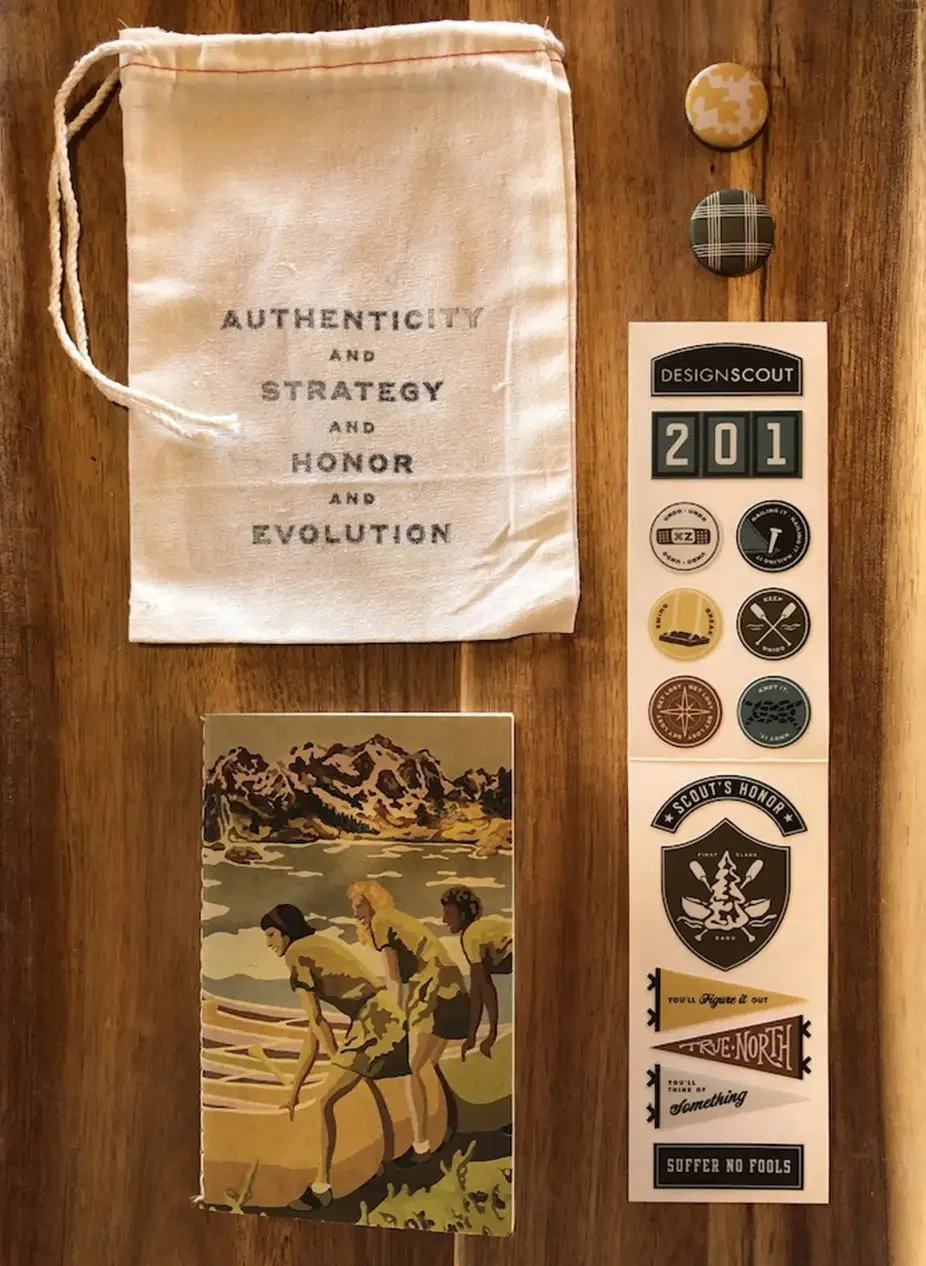 A collection of items on a wooden surface, including a fabric bag with the words 'Authenticity and Strategy and Honor and Evolution,' two round badges, a sticker sheet with Scout-themed designs and the number 201, and a vintage-style illustration of 