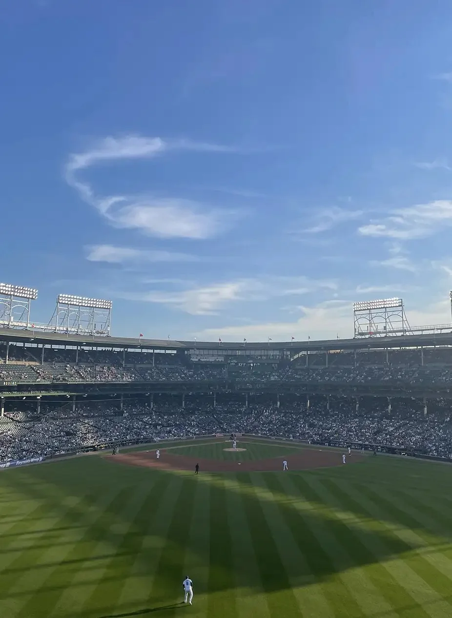 A baseball stadium filled with spectators during a game on a clear day with some clouds in the sky.