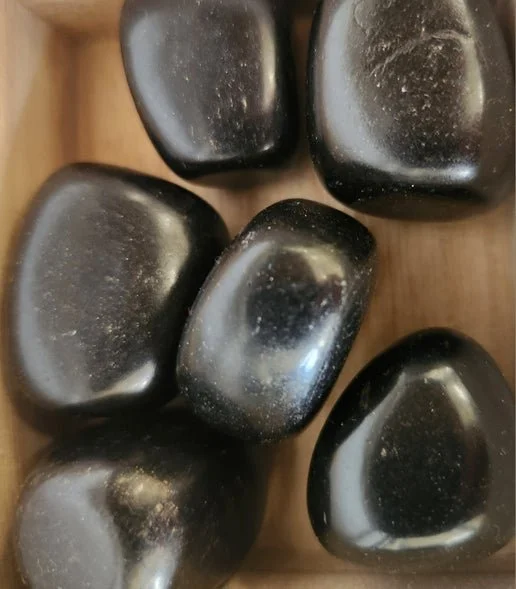Smooth black Jet stone in polished and natural forms, showing lightweight fossilized wood texture.